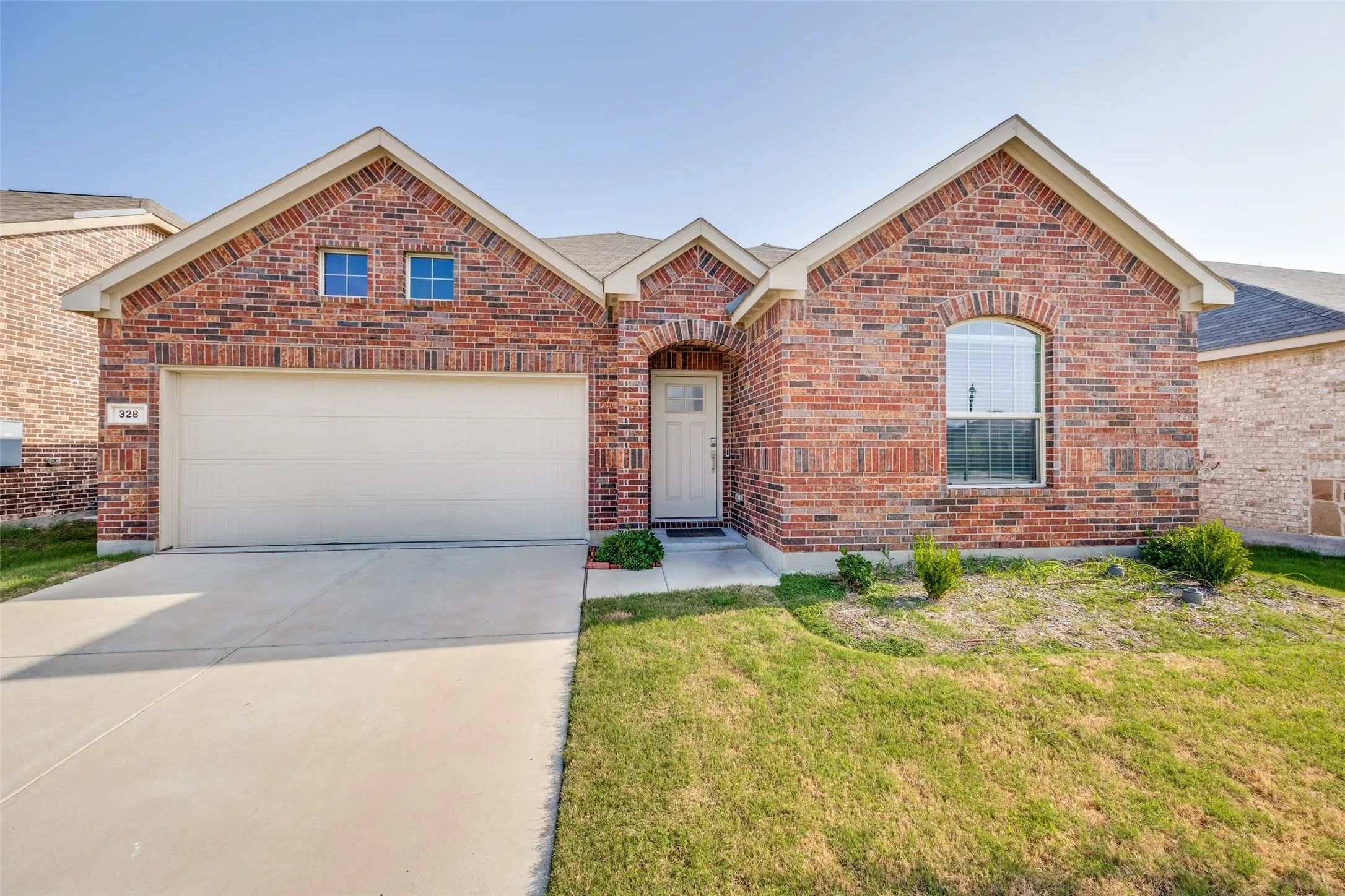 Brick exterior with an arched entry, a two-car garage, a concrete driveway, and a front lawn