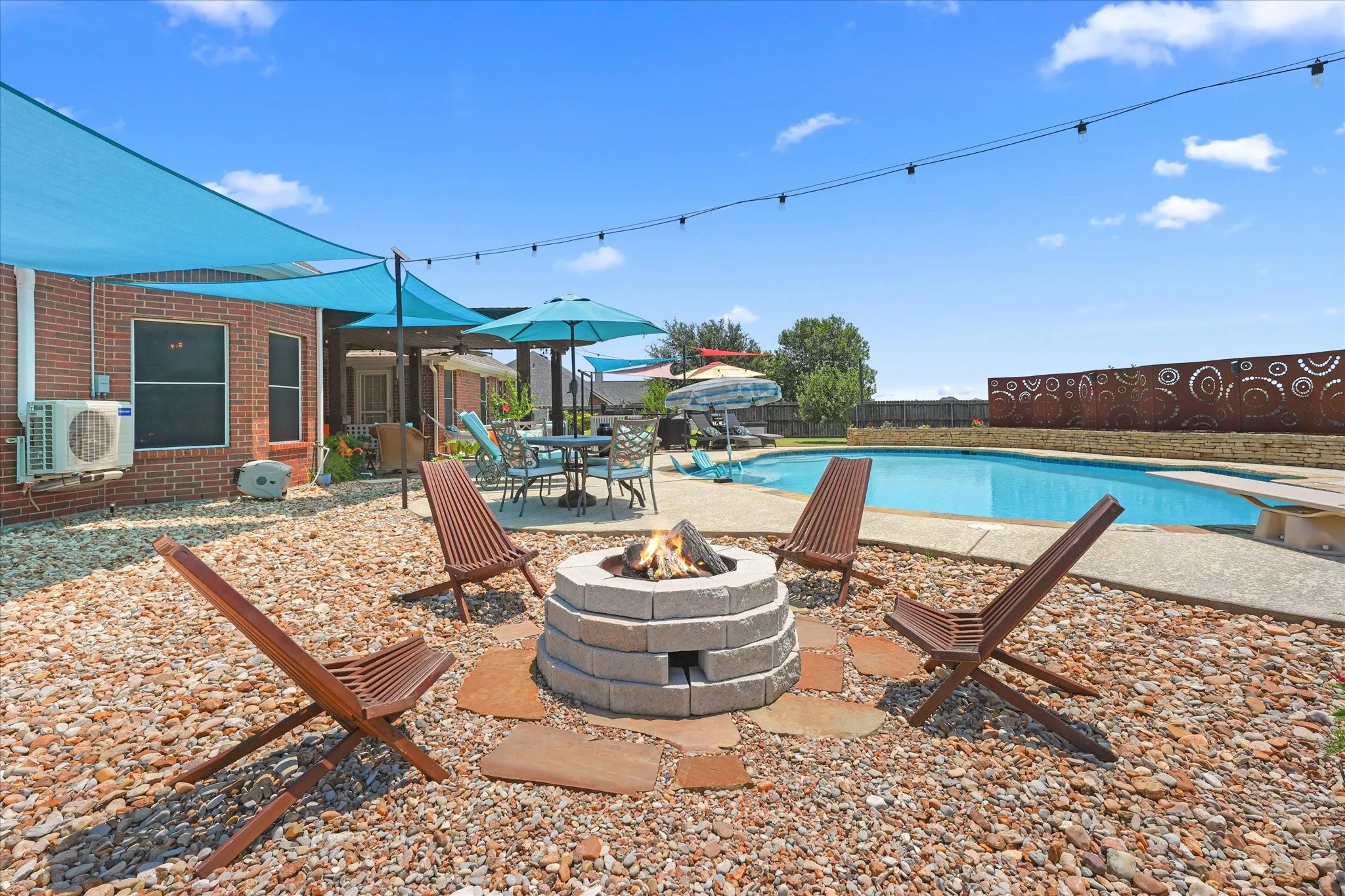 Outdoor living area featuring a stone block fire pit, pebble landscaping, and a in-ground swimming pool with art deco steel privacy wall