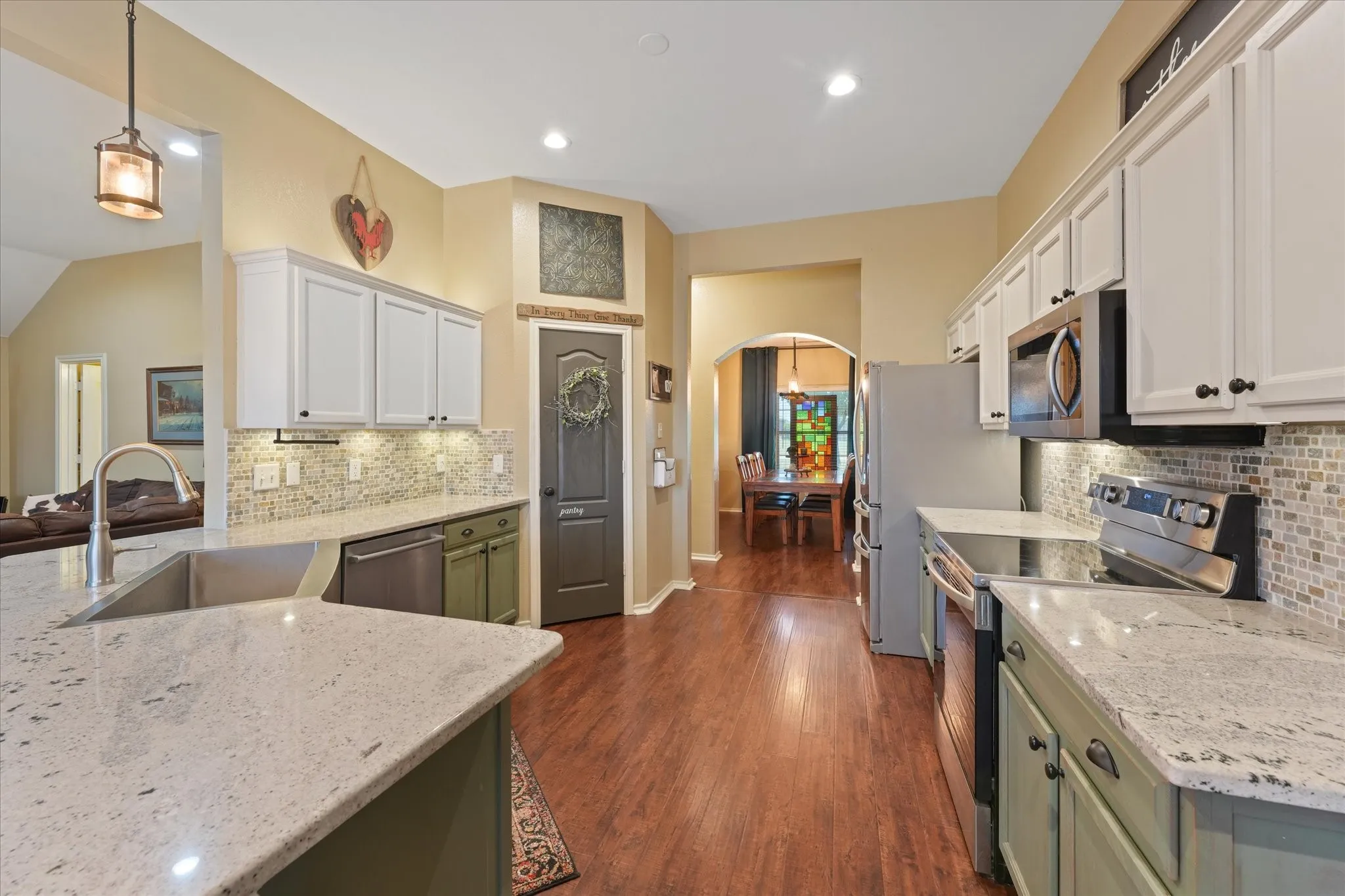 Kitchen featuring wood-finish flooring, two-tone cabinetry, stainless steel appliances, granite countertops, and a mosaic tile backsplash