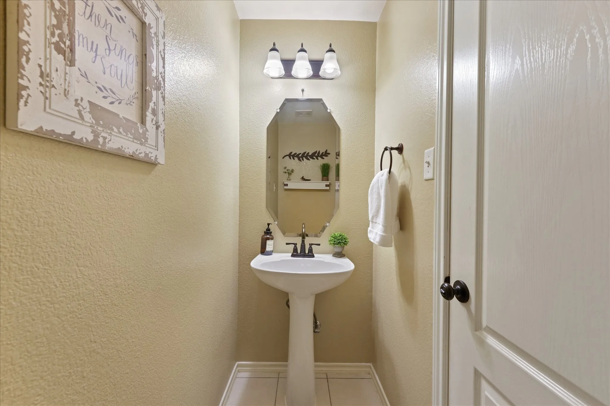Half bathroom with a pedestal sink, an octagonal mirror and three-light vanity fixture