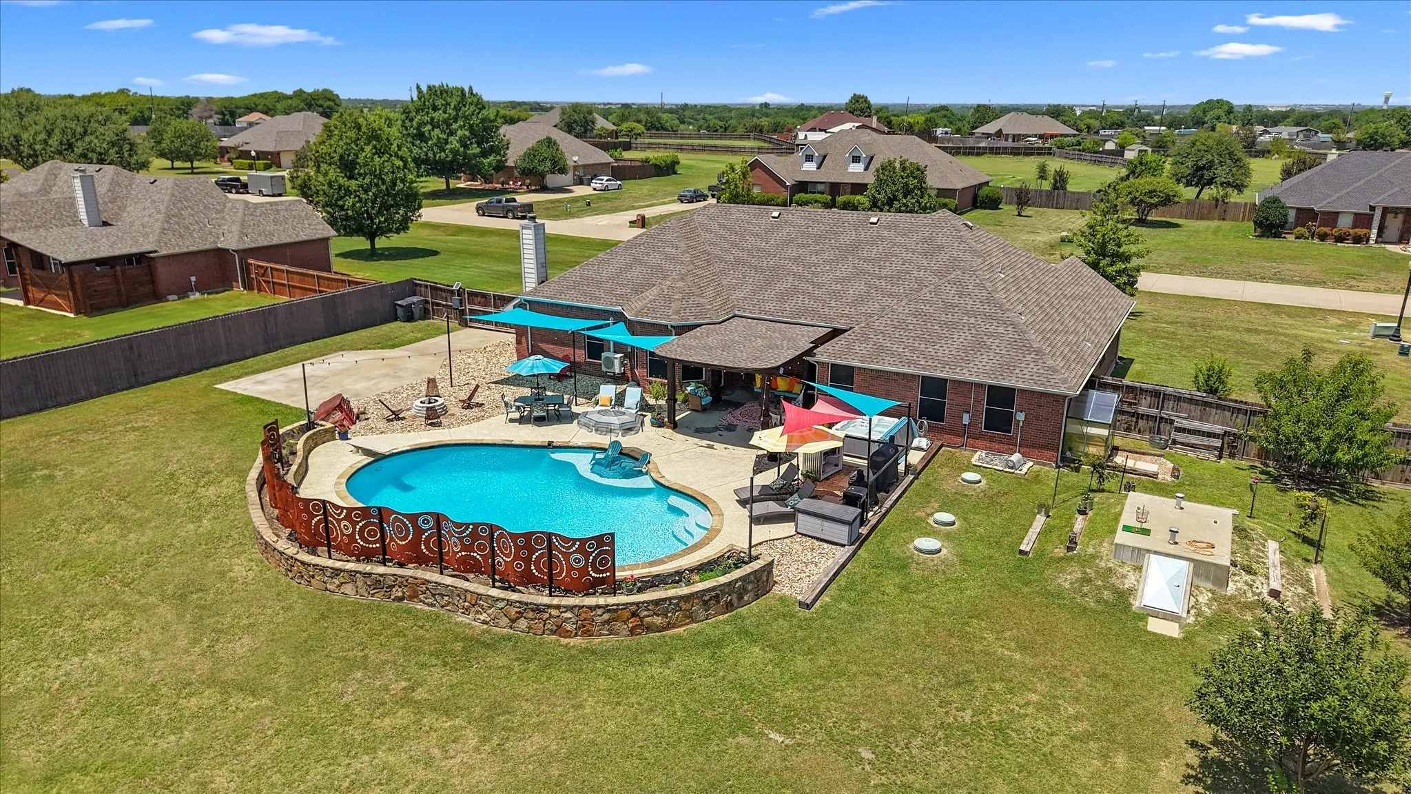 Rear exterior featuring a brick facade, shingled roof, additional parking, covered patio, in-ground swimming pool with art deco steel privacy wall, outdoor cooking area and walk-in storm shelter