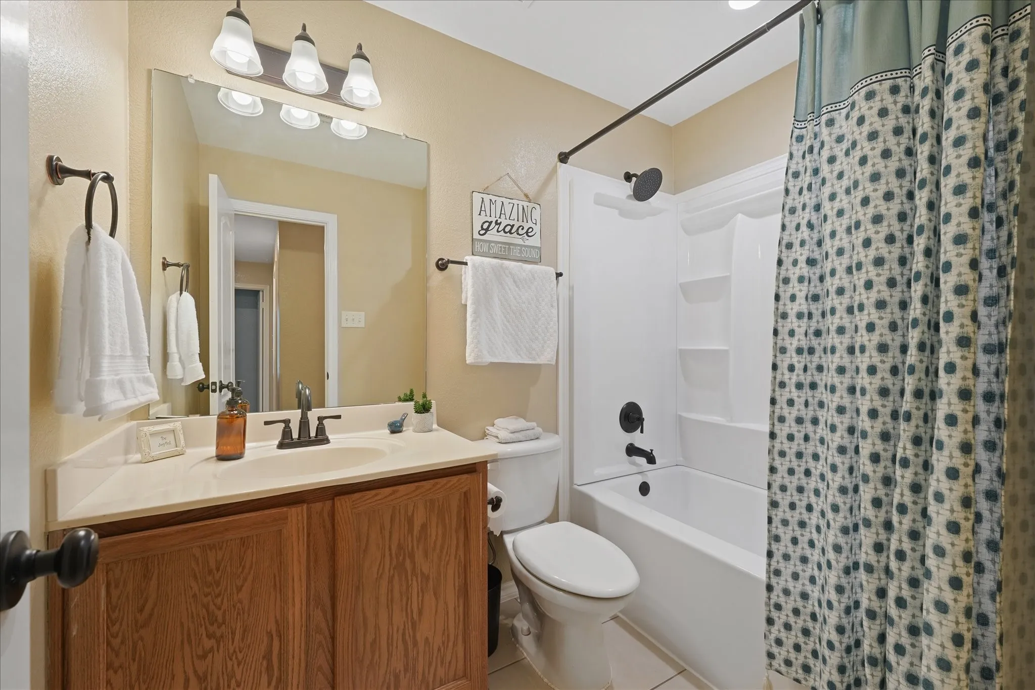 Full guest bathroom featuring a wood-finish vanity with a light-toned countertop, an undermount sink, and a three-light vanity fixture