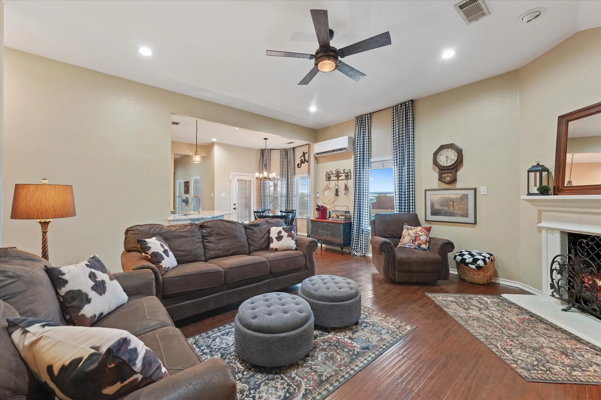 Spacious living area featuring wood-finish flooring, a traditional fireplace with a decorative white mantel, recessed lighting, and a ceiling fan