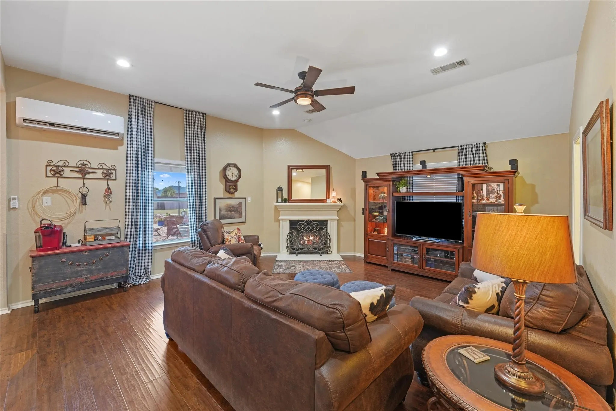 Living area featuring wood-finish flooring, fireplace with decorative mantle, a vaulted ceiling, ceiling fan, and recessed lighting