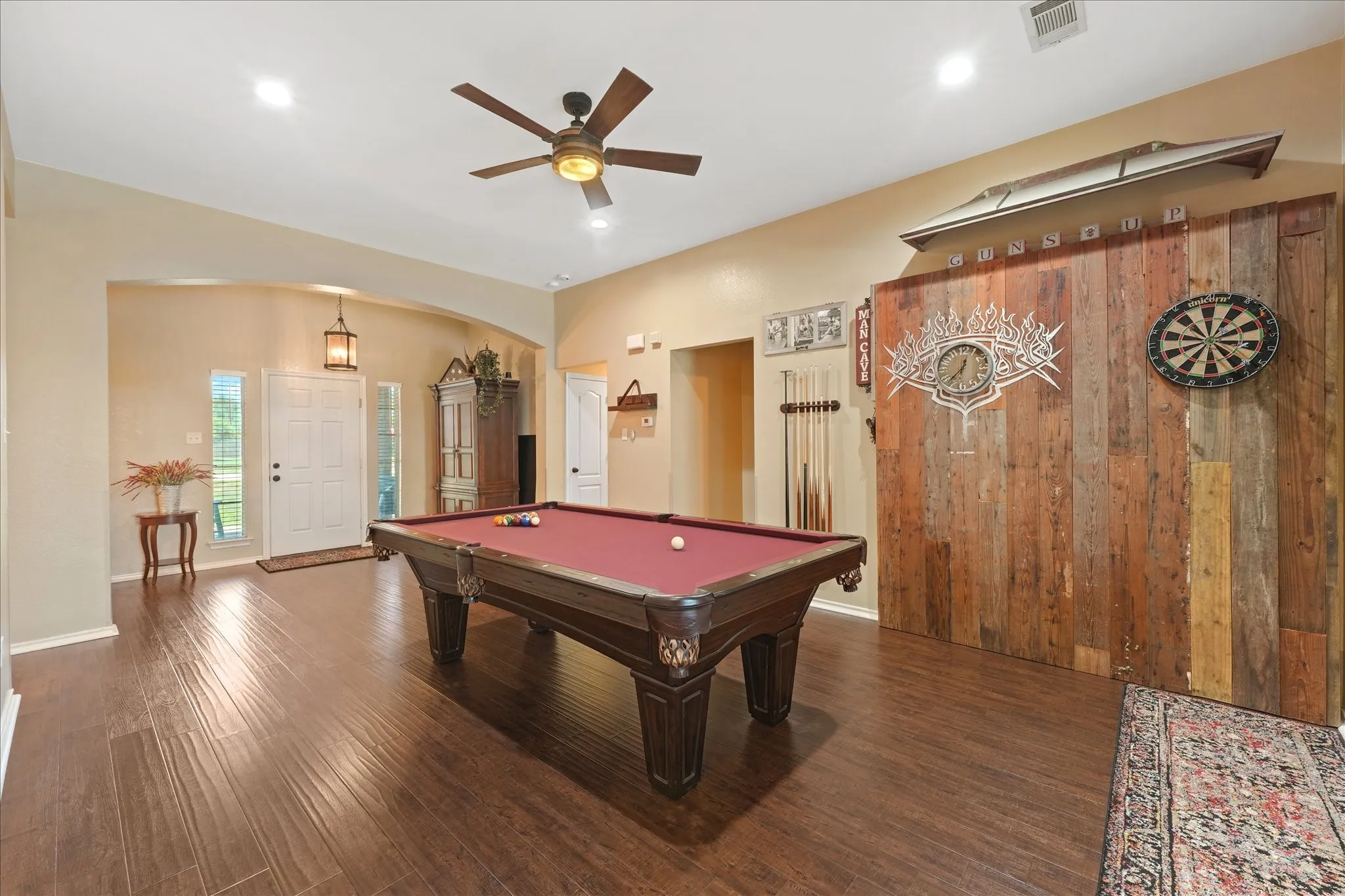 Spacious room featuring wood-finish flooring, a ceiling fan with integrated lighting, recessed lighting, and a prominent reclaimed wood accent wall