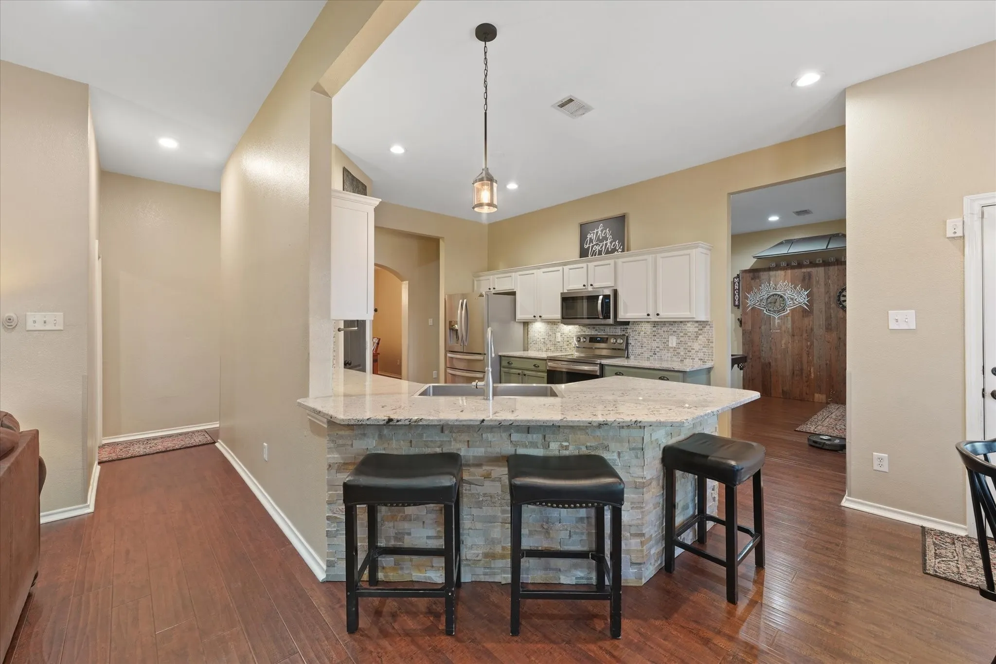 Kitchen featuring a peninsula with stone veneer base and light-toned, granite countertop, stainless steel appliances, white upper cabinetry, and a decorative mosaic tile backsplash