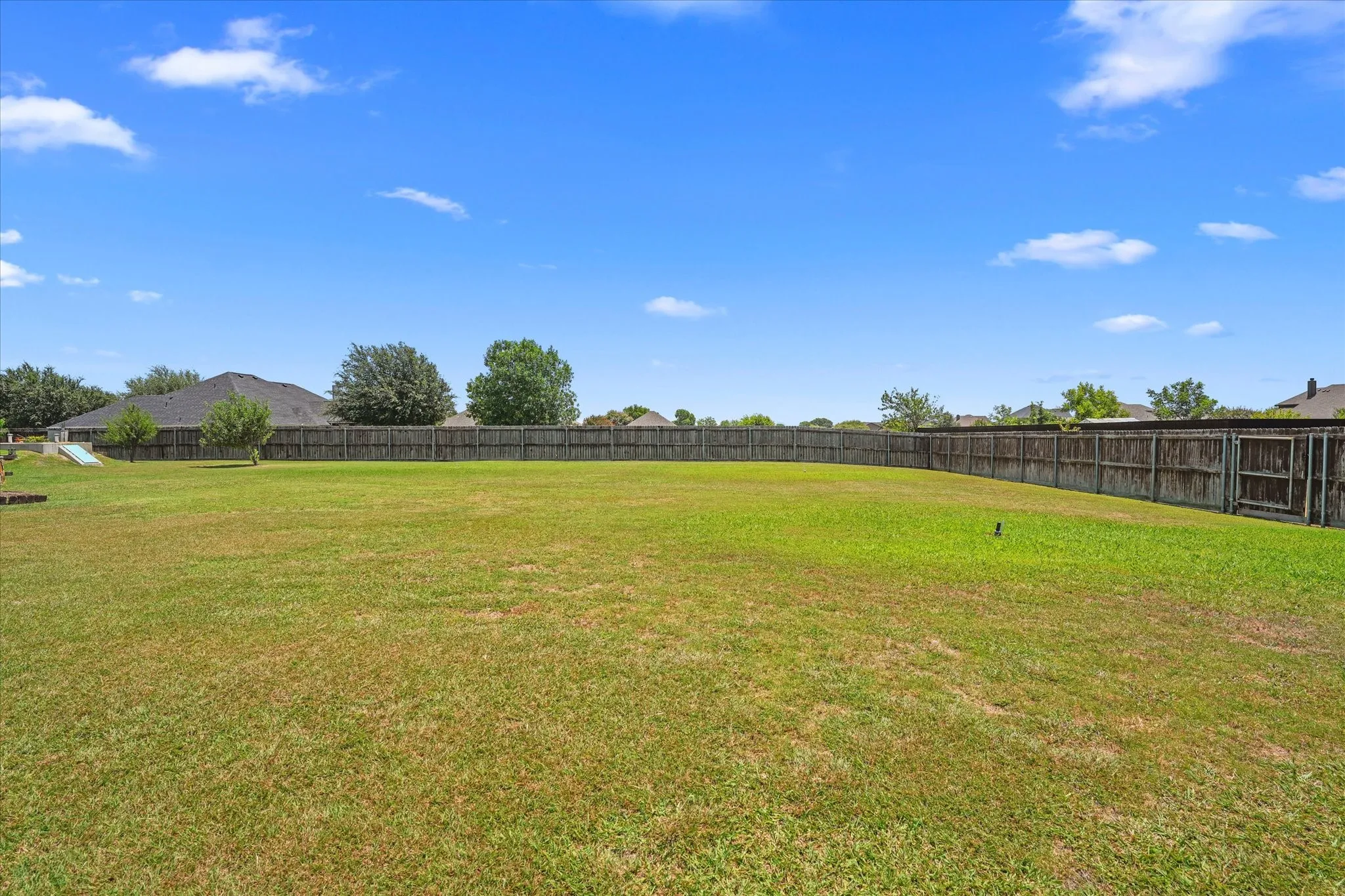 Expansive backyard featuring a manicured lawn, a wood fence surrounding the perimeter, and mature trees