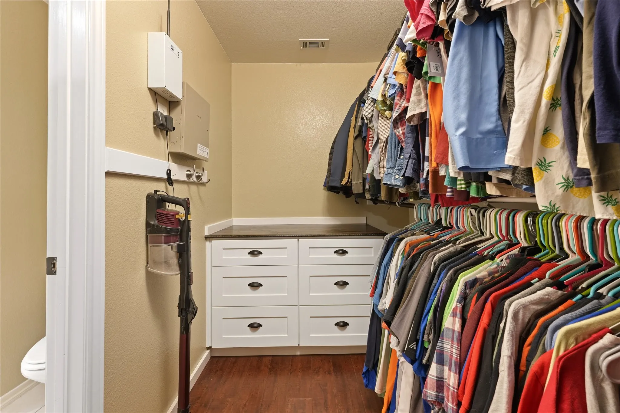 Walk-in closet featuring wood-finish flooring, built-in white cabinetry with dark hardware, and integrated hanging rods
