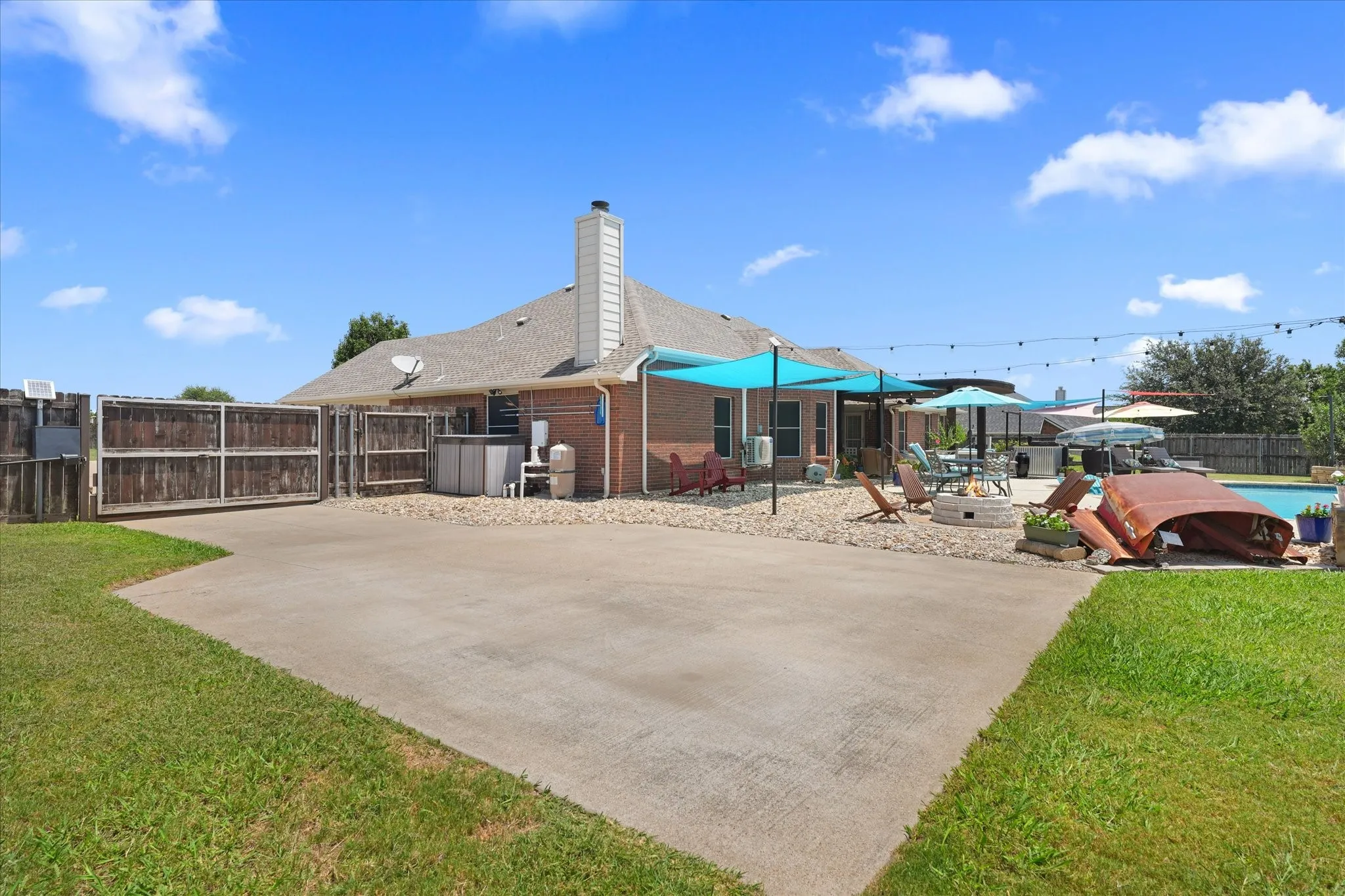 Expansive concrete area for additional parking, in ground pool, fire pit, electric gate and manicured green lawn
