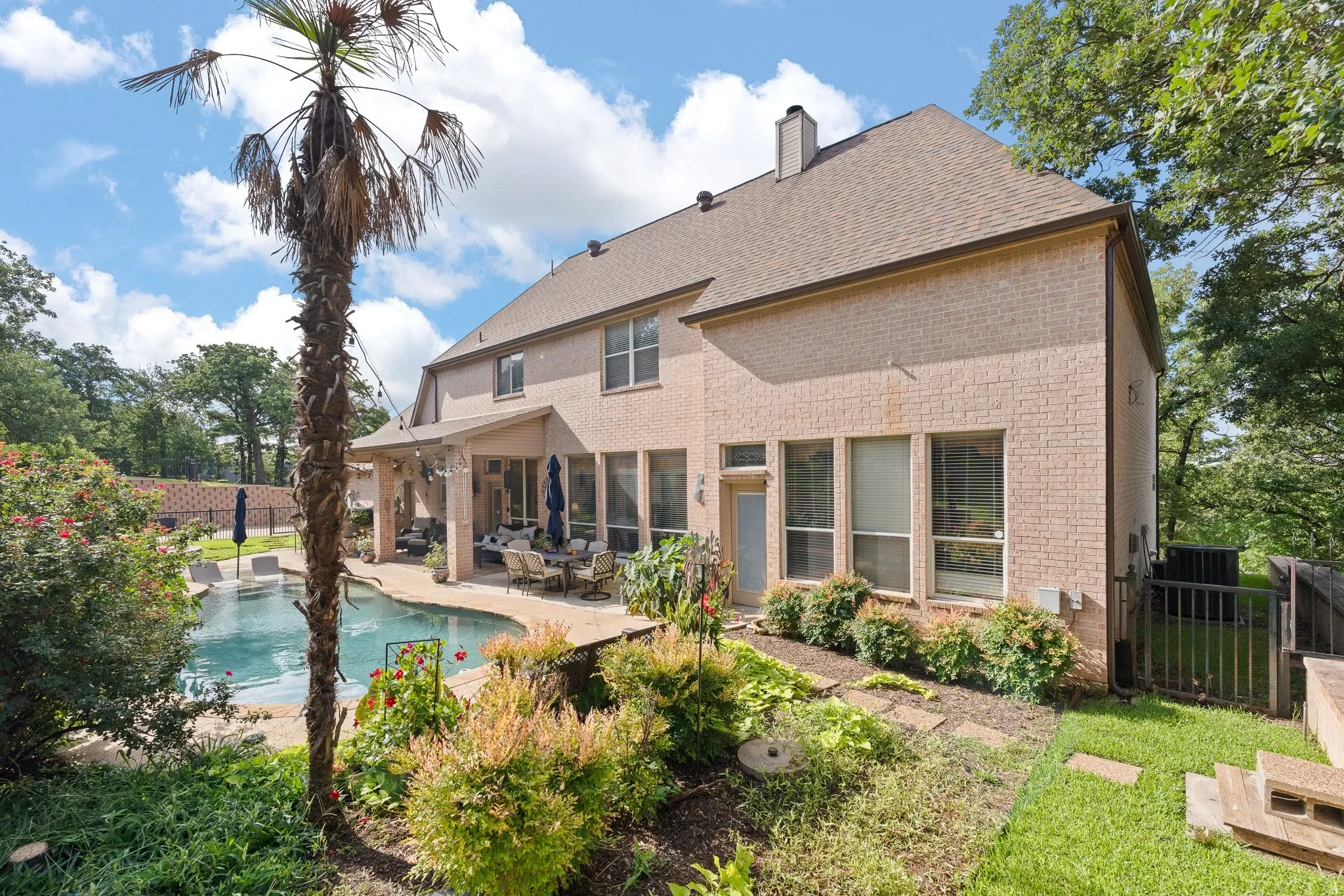 Rear exterior featuring a light-colored brick facade, a covered patio, and an inground swimming pool