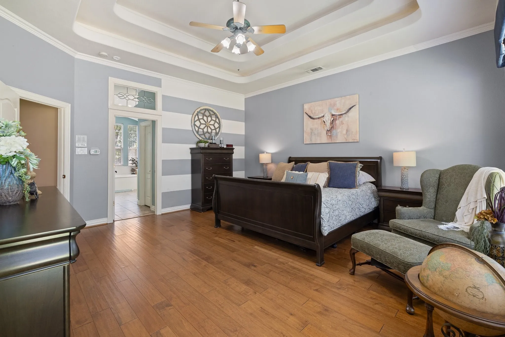 Spacious room featuring wood-finish flooring, a tray ceiling with a ceiling fan, and light blue walls