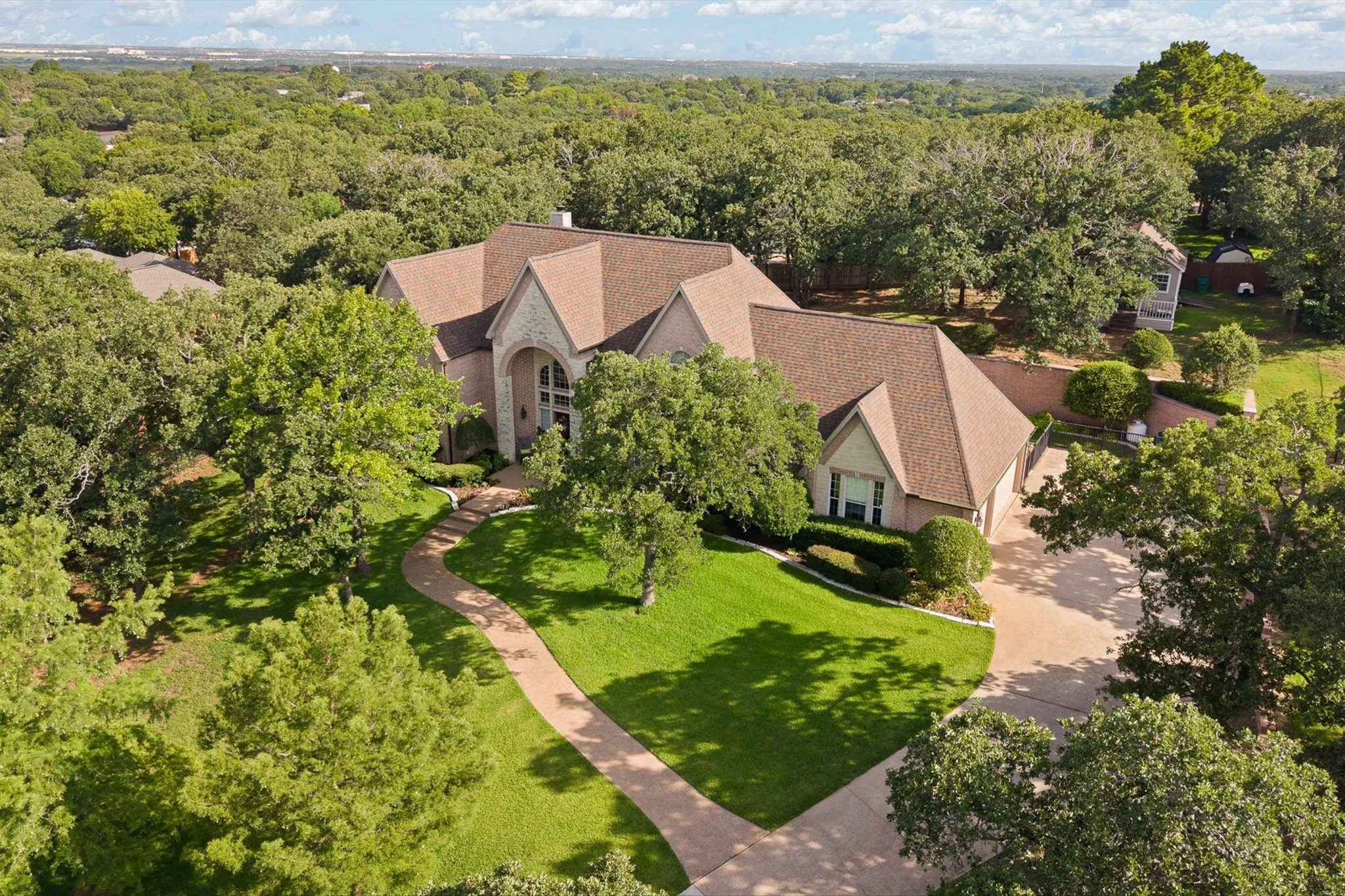 Expansive property featuring a stone and stucco exterior, a winding paved walkway, mature trees, a manicured lawn, and a multi-car driveway