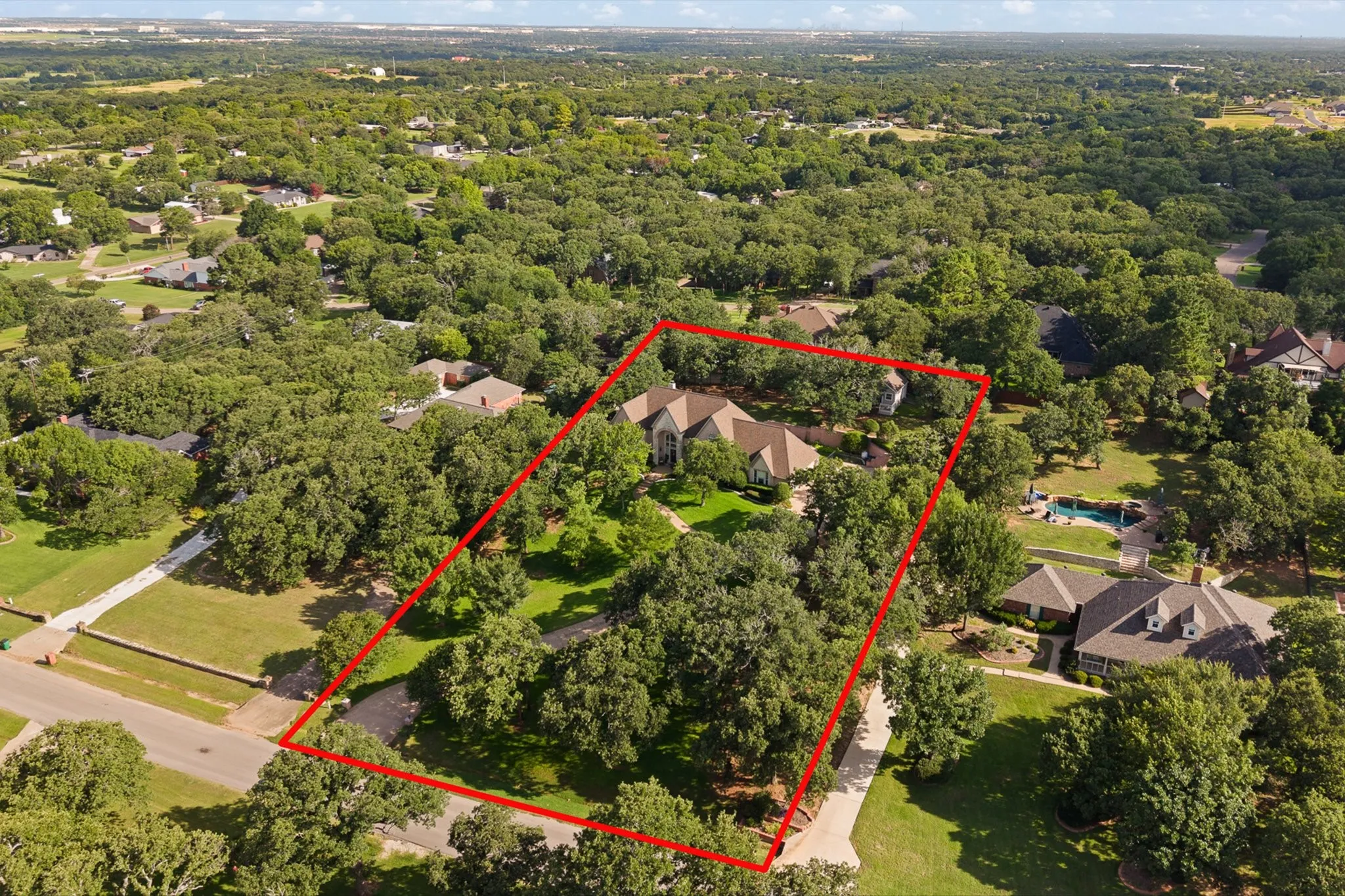 Expansive property featuring a single-story residence with a multi-gabled roof and a tree-lined perimeter