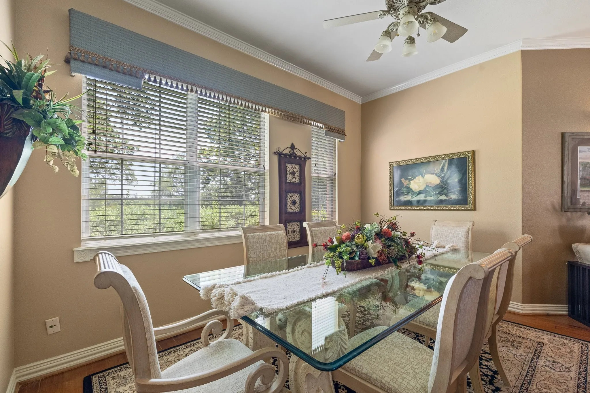 Dining area featuring a large window with custom cornice board, crown molding, wood flooring, and a ceiling fan with integrated lighting