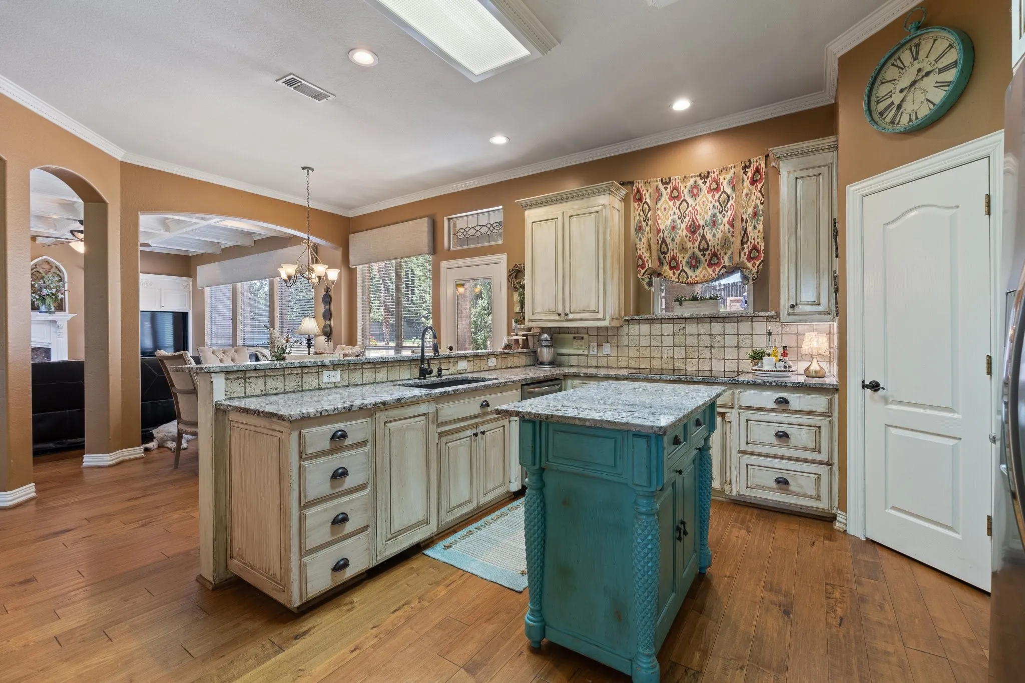 Expansive kitchen featuring wood-finish flooring, light-toned cabinetry, granite countertops, and a central island with a contrasting finish