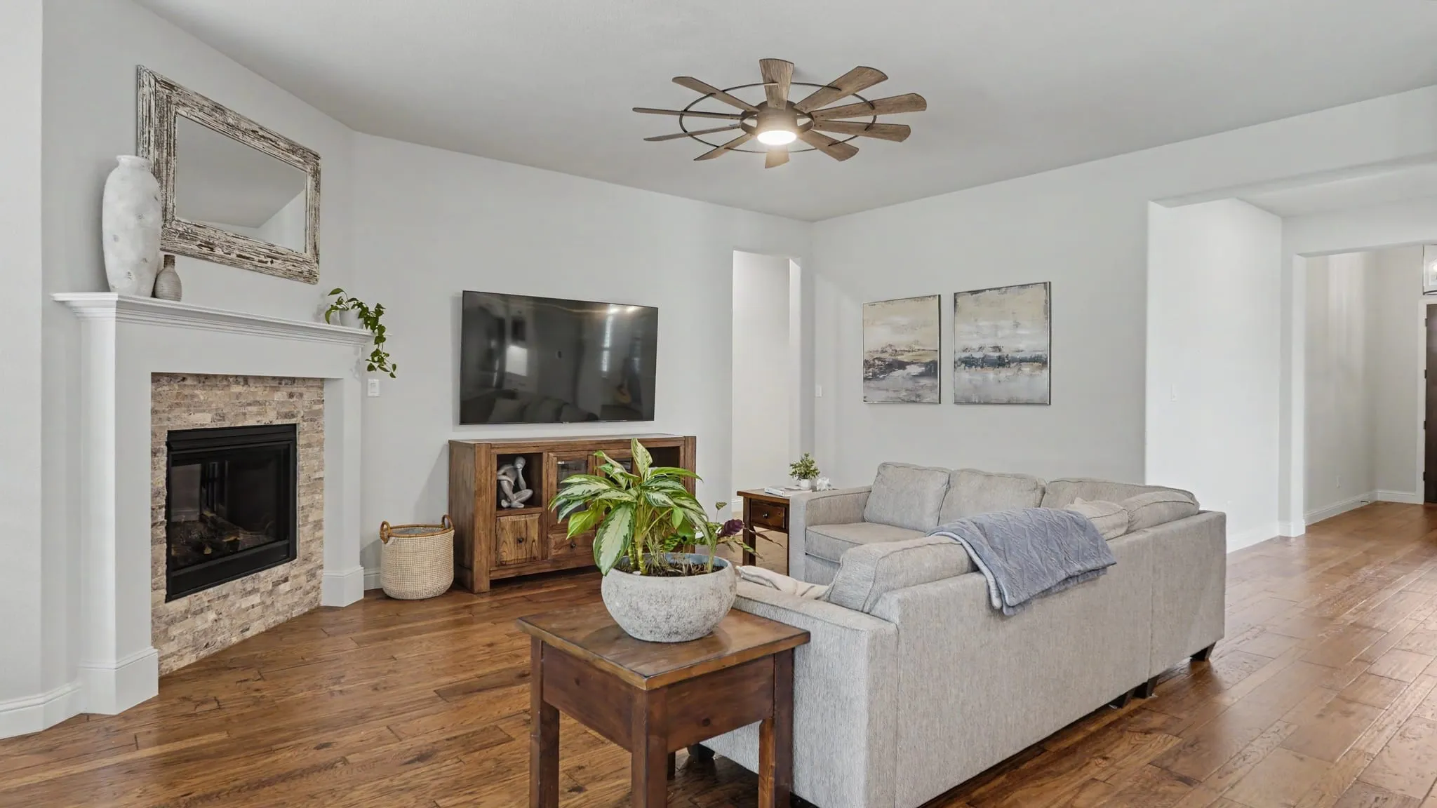 Living area featuring hardwood floors, a corner fireplace with a stone surround and white mantel, and a ceiling fan with integrated lighting.