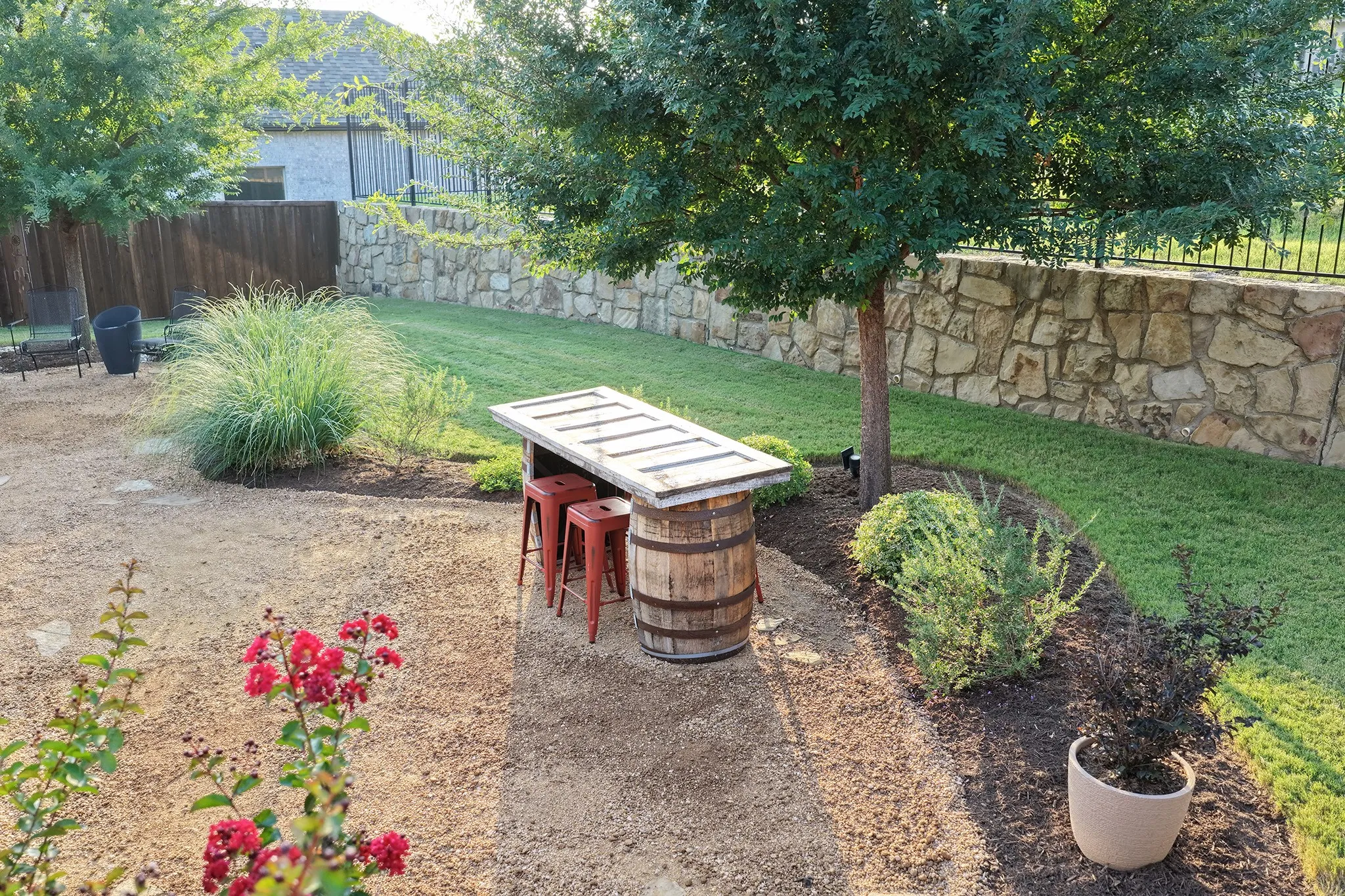 Expansive backyard with a stone retaining wall, wrought iron fencing, and a manicured lawn, with a shade tree.