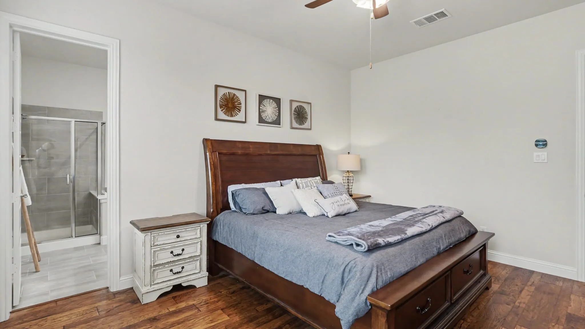 Bedroom featuring hardwood floors, three windows with white plantation shutters, and a ceiling fan with integrated lighting.