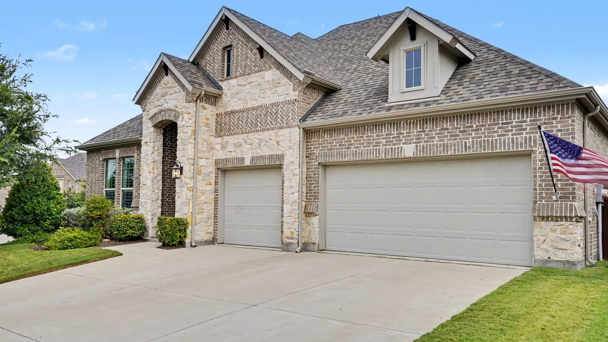 Three-car garage with light gray doors and a multi-textured brick and stone facade.
