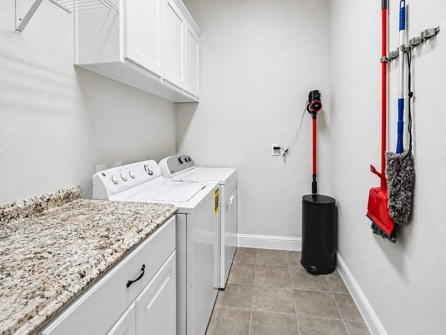 Dedicated laundry area featuring a granite-style countertop, white cabinetry with dark hardware, and neutral tile flooring, and extra cabinet space.