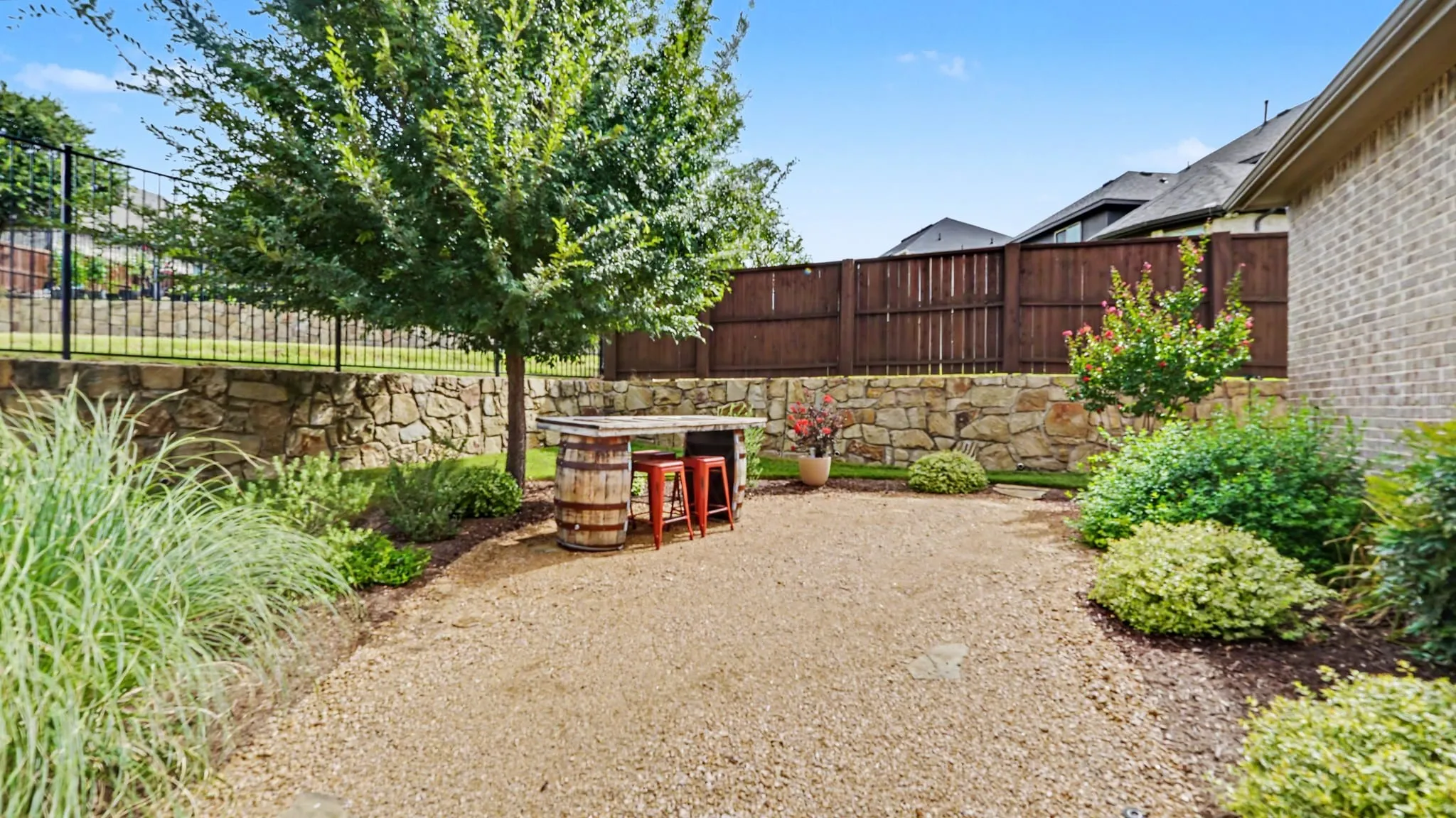Expansive decomposed granite patio with a stone retaining wall and mature perimeter landscaping, and a shade tree.