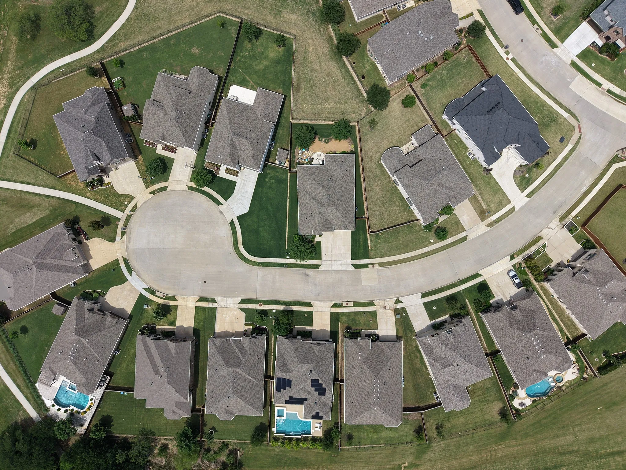 Aerial view of a residential cul-de-sac with multiple properties featuring shingle roofs, green lawns, and paved driveways.