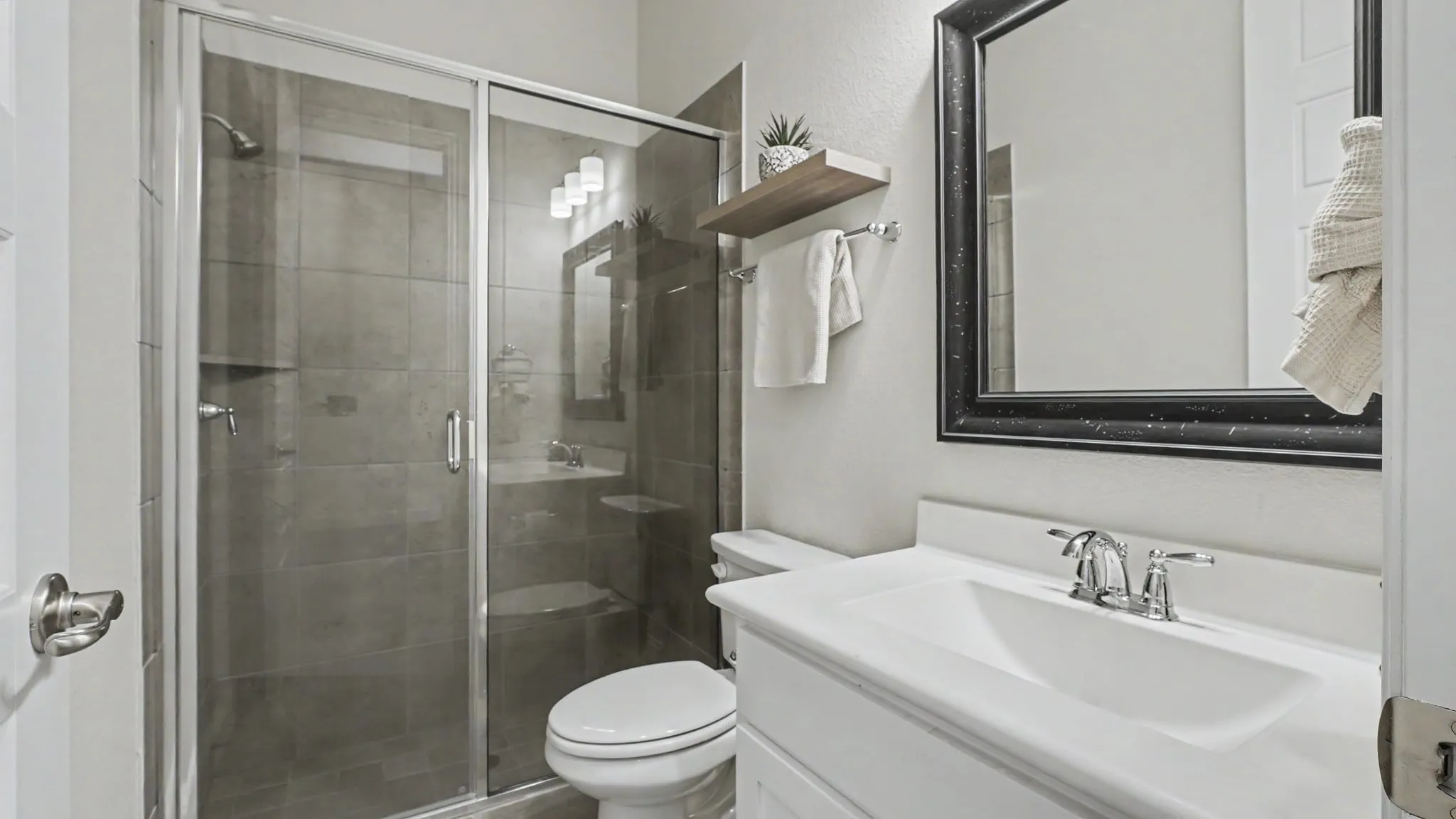 Bathroom featuring a glass-enclosed walk-in shower with large tile, a single vanity with an integrated sink, chrome fixtures, and a framed mirror.
