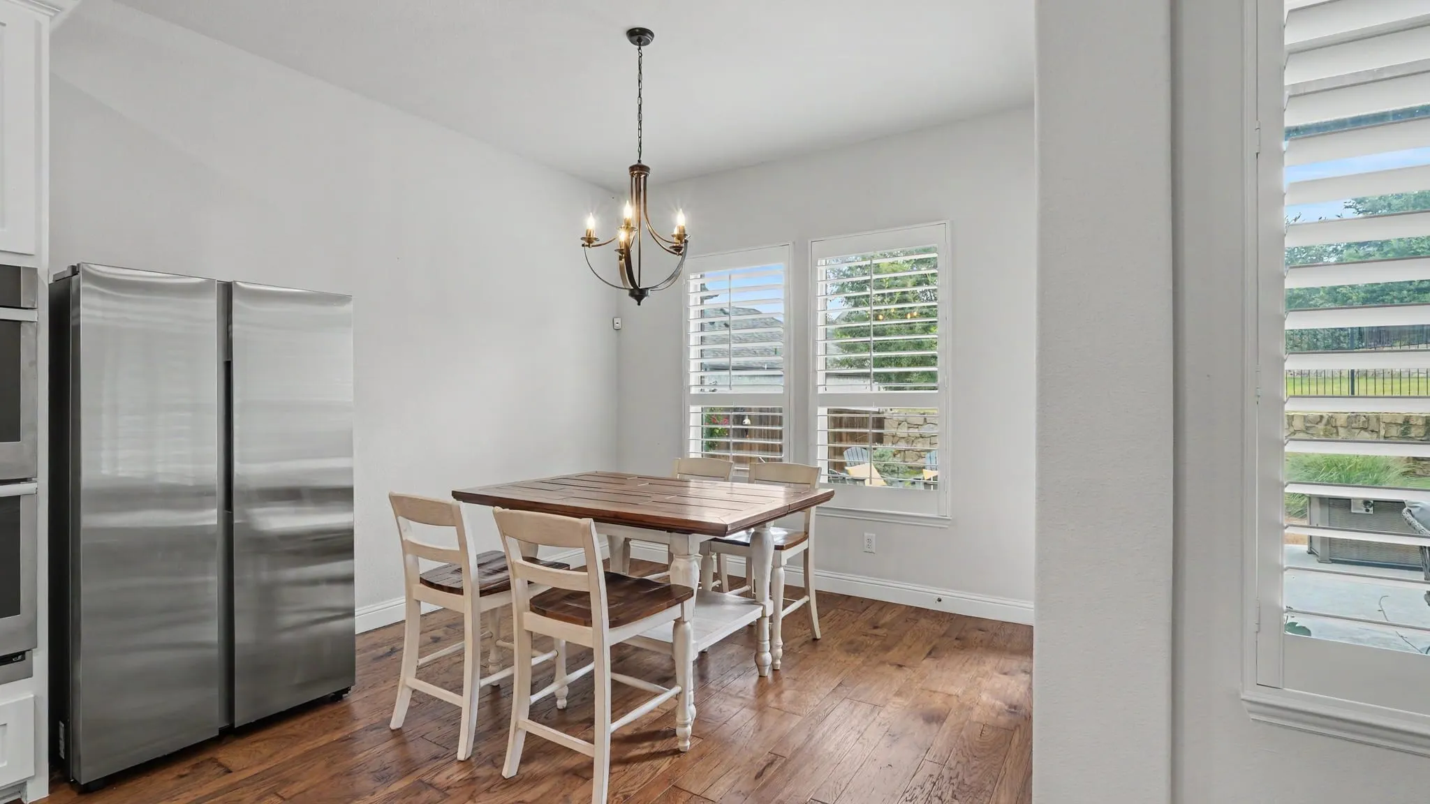 Dining area featuring hardwood floors, two large windows with plantation shutters, and a dark bronze chandelier.