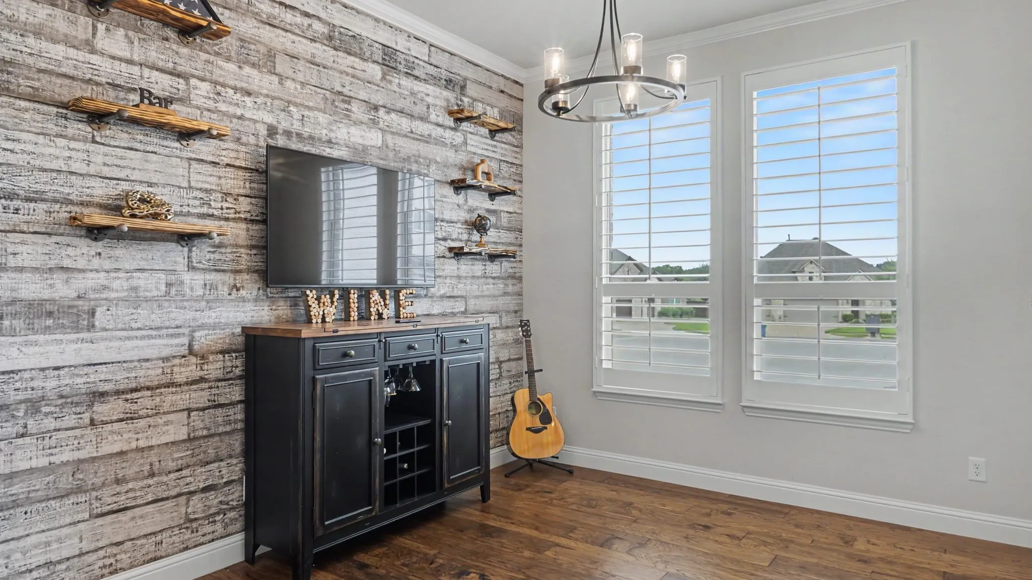 Formal dining/bar/sitting area with custom shiplap wall and industrial farmhouse style shelves, showcasing hardwood floors and plantation shutters that overlook cul de sac. Could easily be converted to an enclosed room or office.