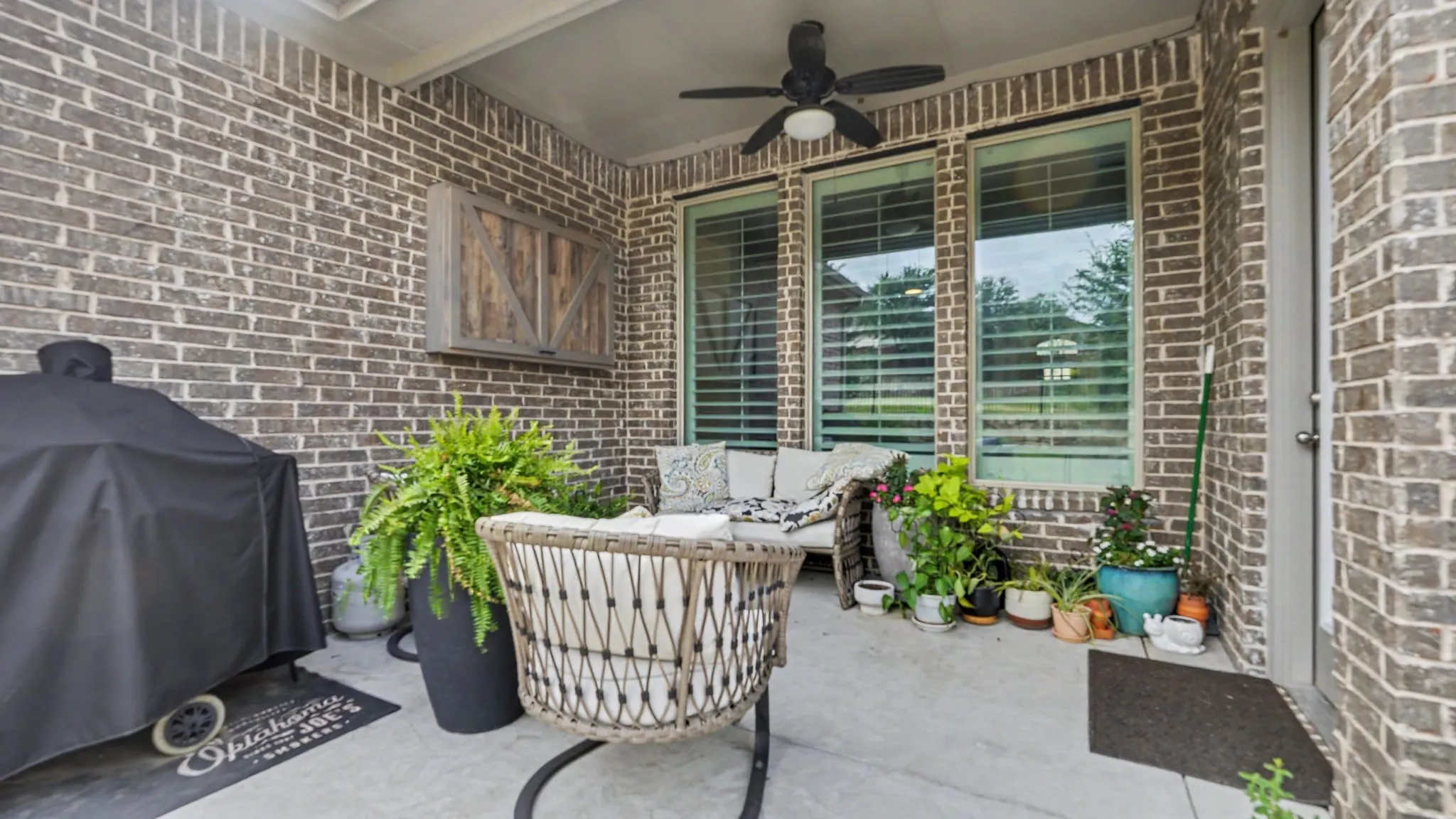 Covered outdoor patio featuring a brick exterior wall, concrete flooring, and a ceiling fan, and a TV mount cabinet.