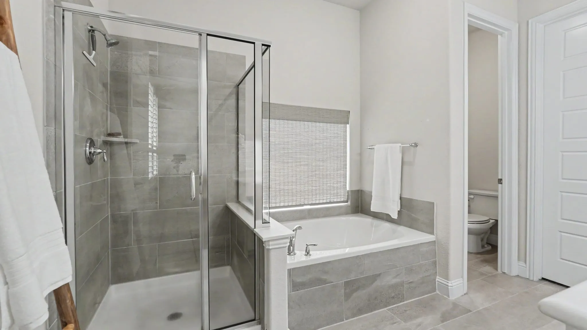 Bathroom featuring a glass-enclosed shower with a tiled surround, a built-in garden bathtub with a tiled facade, chrome fixtures, and light-toned floor tiling, and separate closed space with toilet.