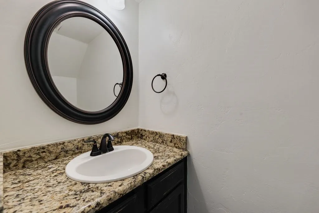 Bathroom vanity featuring a granite countertop, undermount sink, dark bronze faucet, and a large oval mirror with a dark frame