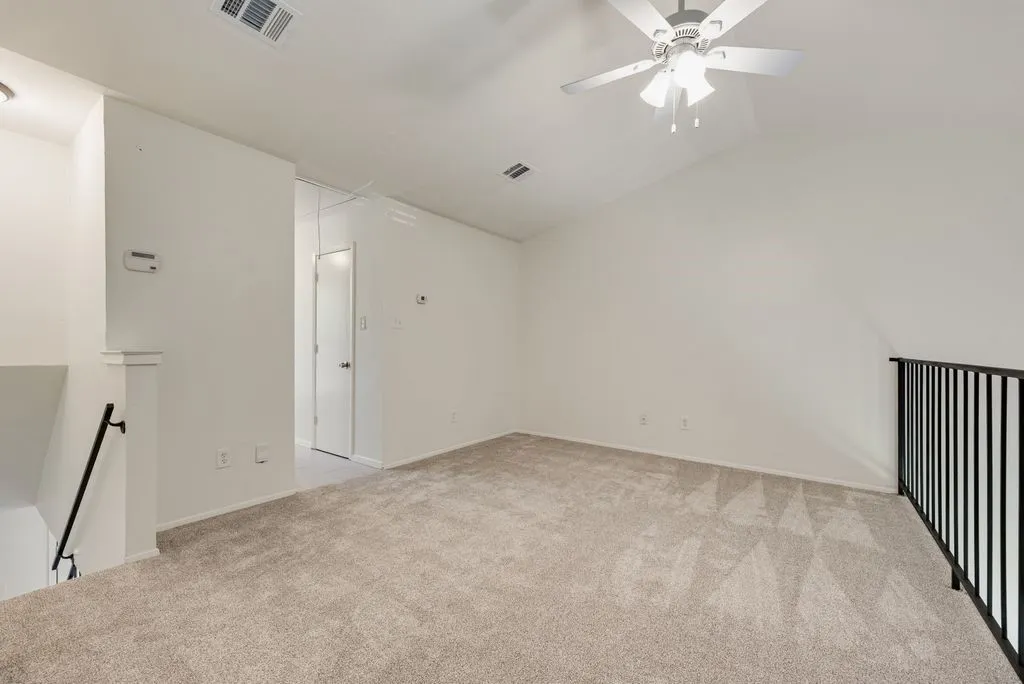 Carpeted loft space featuring an angled ceiling, ceiling fan, and black metal railing overlooking a lower level