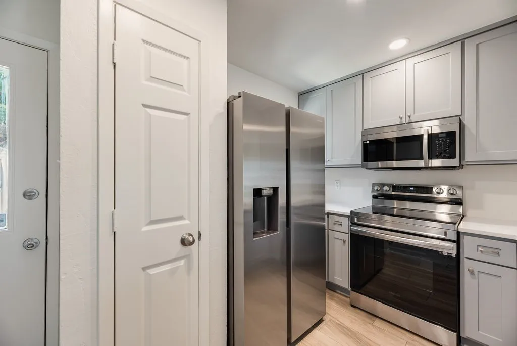 Contemporary kitchen featuring stainless steel appliances, light gray cabinetry, white countertops, and wood-finish flooring