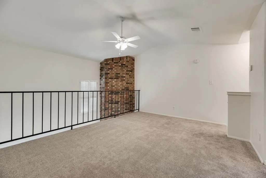 Open loft area featuring neutral-tone carpeting, a white ceiling fan, and a partial brick accent wall
