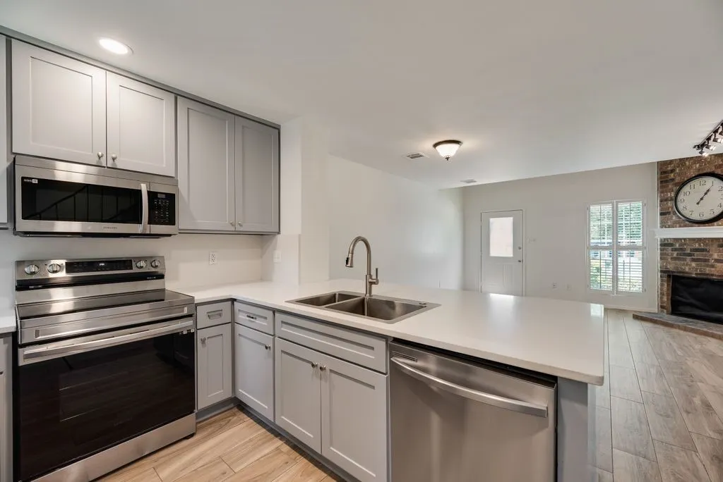 Modern kitchen featuring light gray cabinetry, stainless steel appliances, a double basin sink, and wood-finish flooring