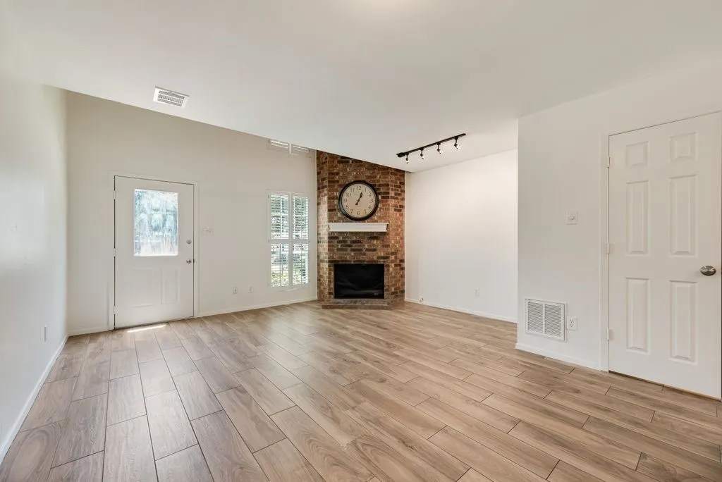 Spacious interior featuring wood-finish flooring, a vaulted ceiling, and a brick fireplace with a white mantel
