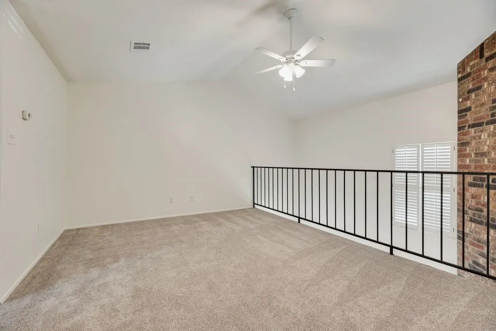 Carpeted loft space featuring an angled ceiling, ceiling fan, and black metal railing overlooking shuttered windows