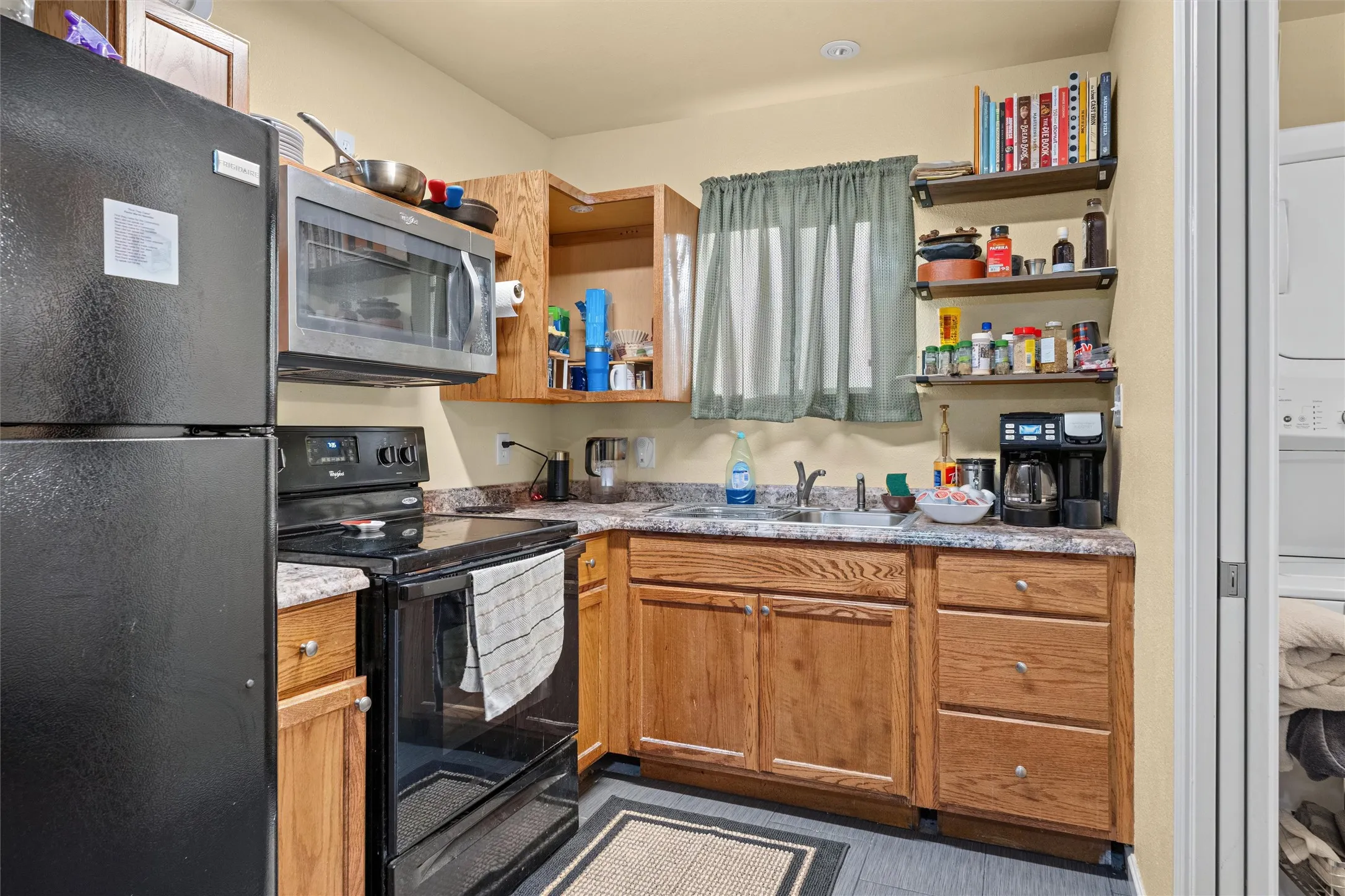 Compact kitchen featuring black appliances, wood-finish cabinetry, and solid surface countertops