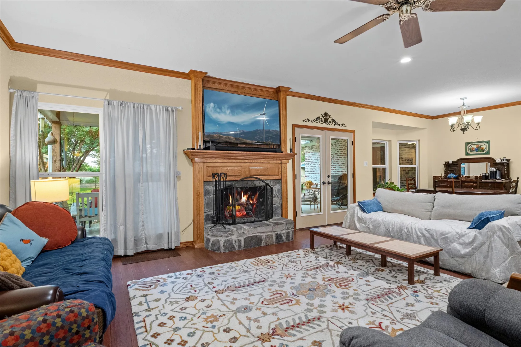 Living area featuring wood-finish flooring, a stone hearth fireplace with a wood mantel, crown molding, and a ceiling fan