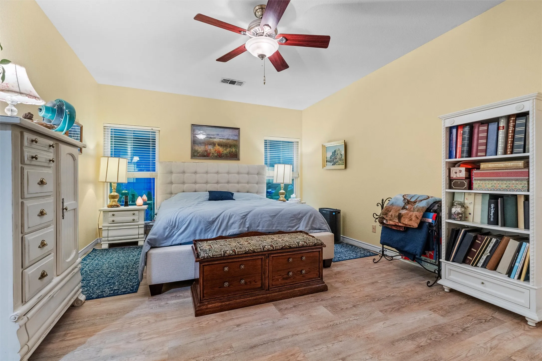 Bedroom featuring vaulted ceilings, wood-finish flooring, two windows with blinds, a ceiling fan, and built-in shelving