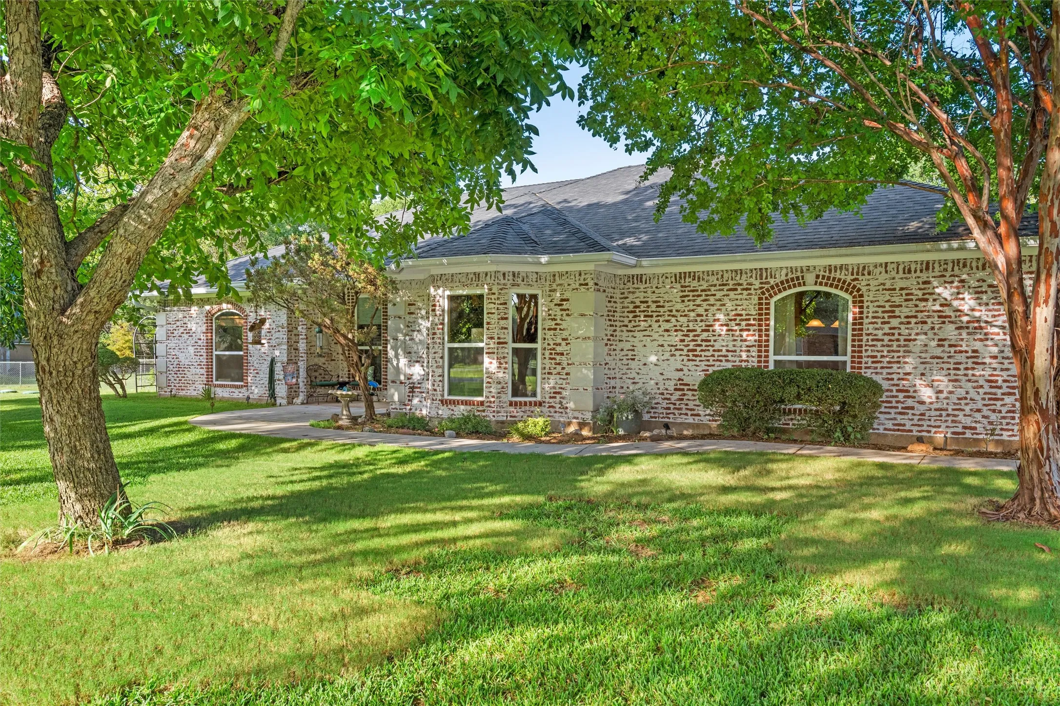 Expansive lawn with mature trees, brick exterior, arched windows, and a paved pathway