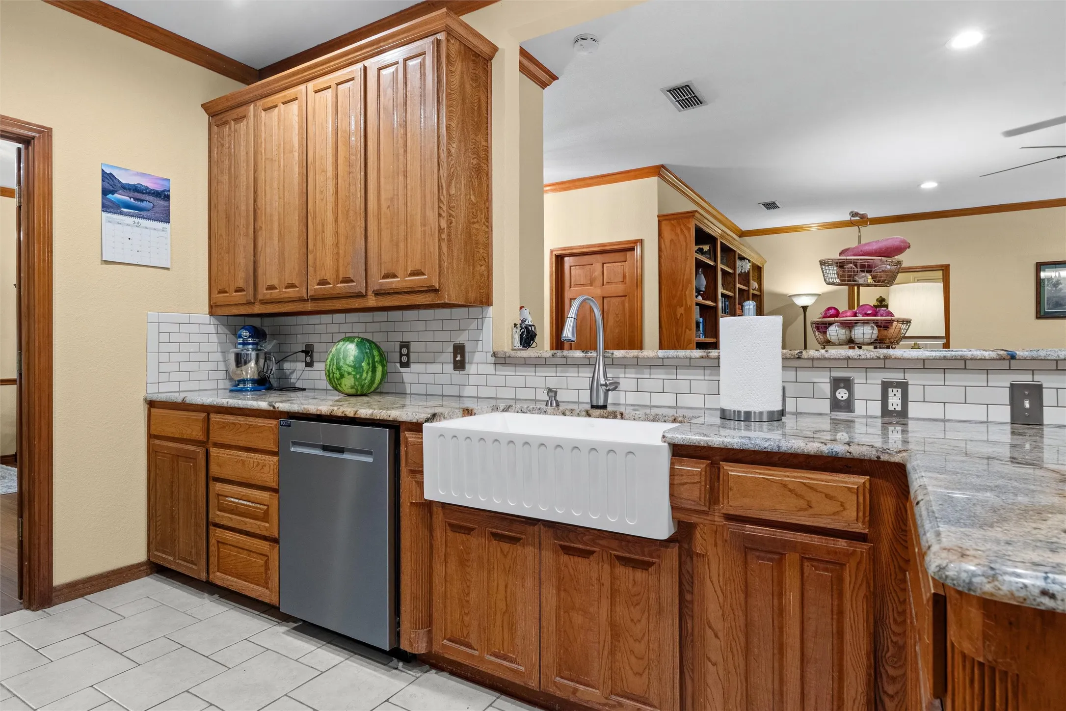 Kitchen featuring a large apron-front sink, granite countertops, subway tile backsplash, stainless steel dishwasher, and wood cabinetry