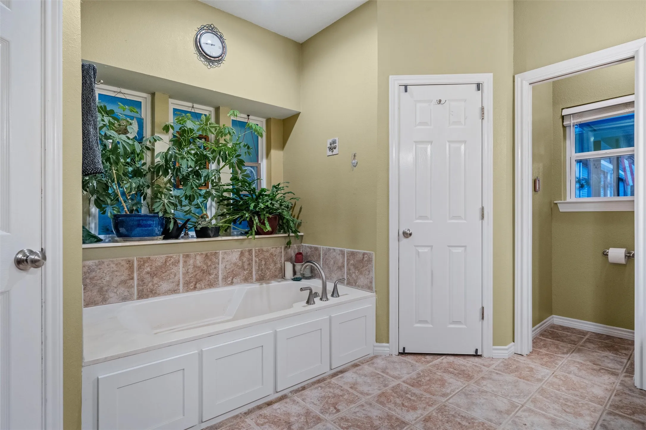 Built-in garden tub with tiled surround, white paneled base, and chrome fixtures