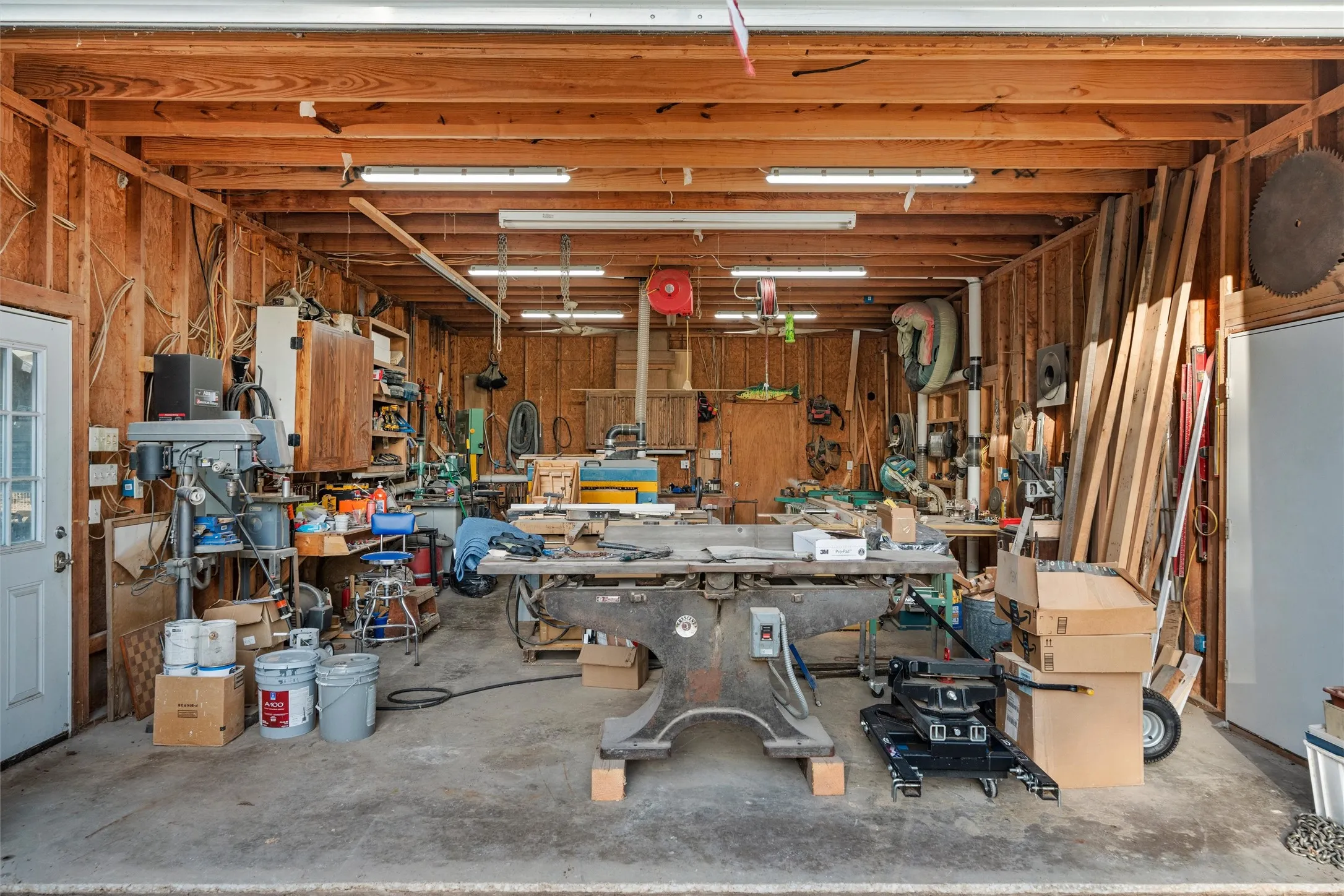 Detached workshop building featuring exposed wood framing, concrete flooring, and multiple fluorescent lighting fixtures