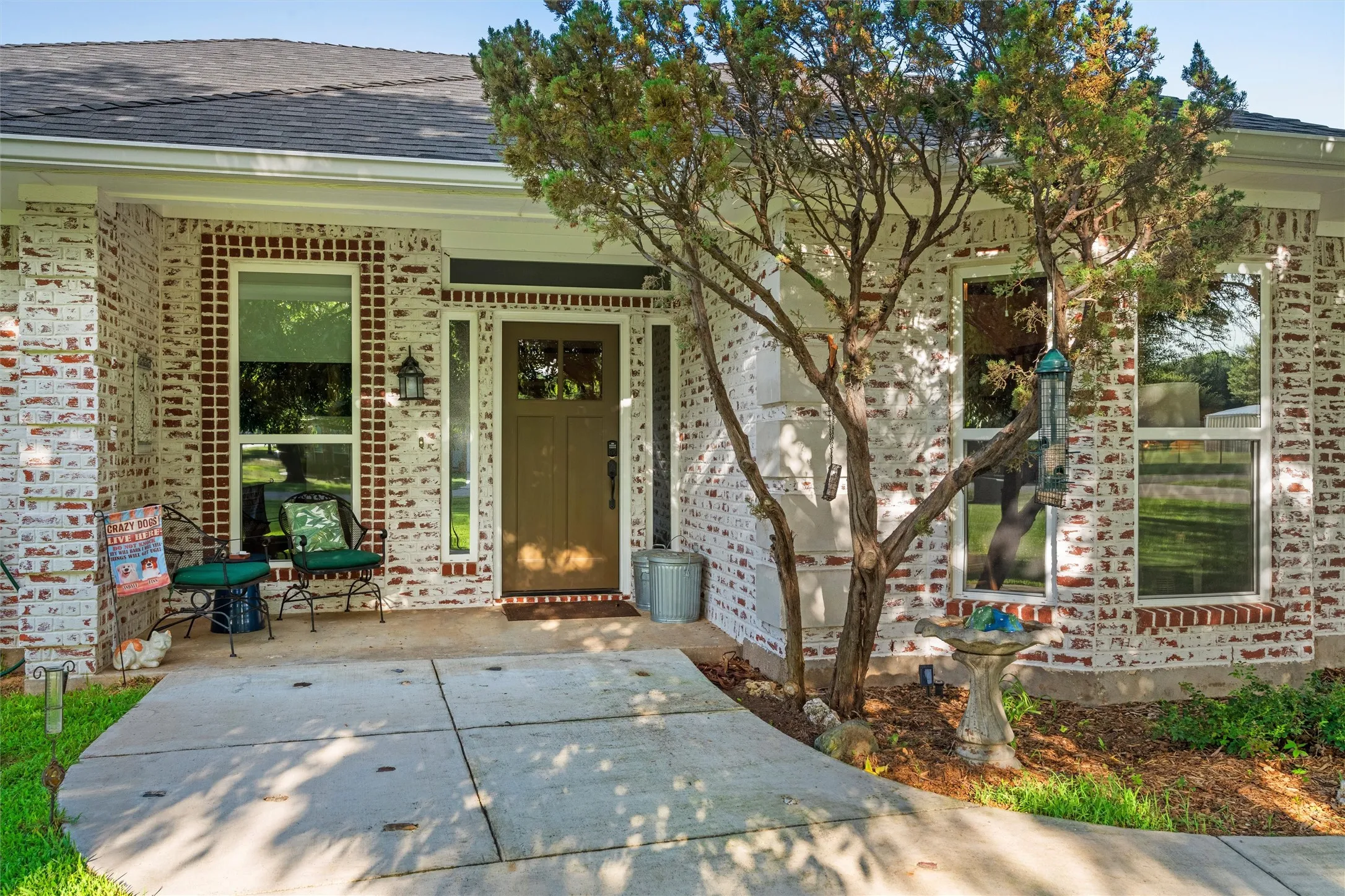 Brick facade with a dark gray shingle roof, a paneled front door, and a concrete pathway