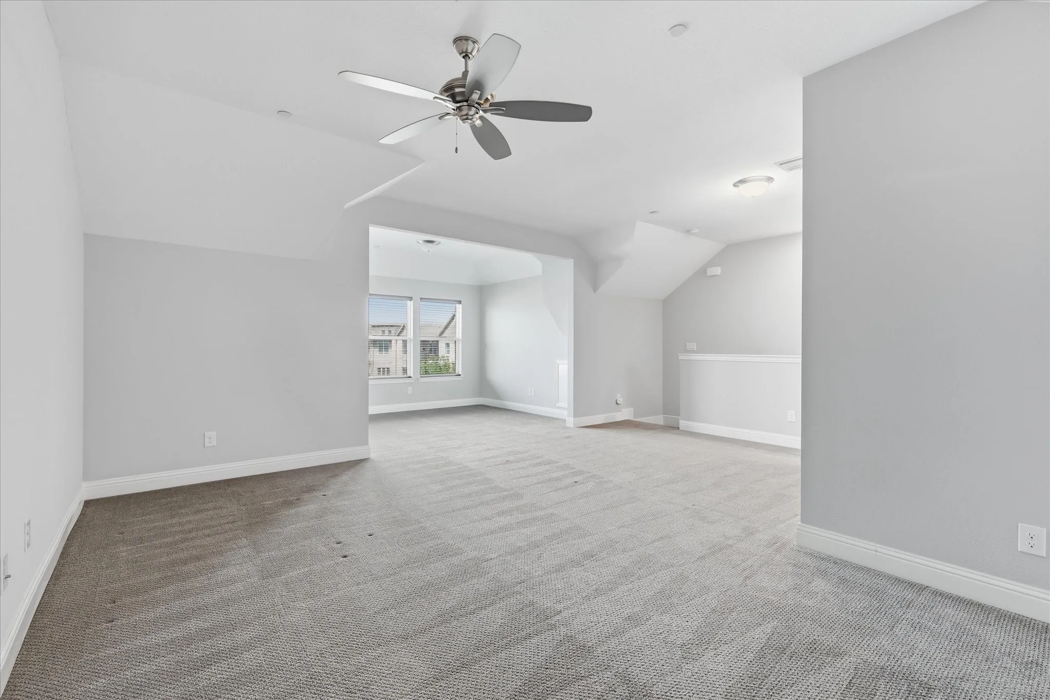 Spacious room featuring sloped ceilings, a ceiling fan, and recessed lighting