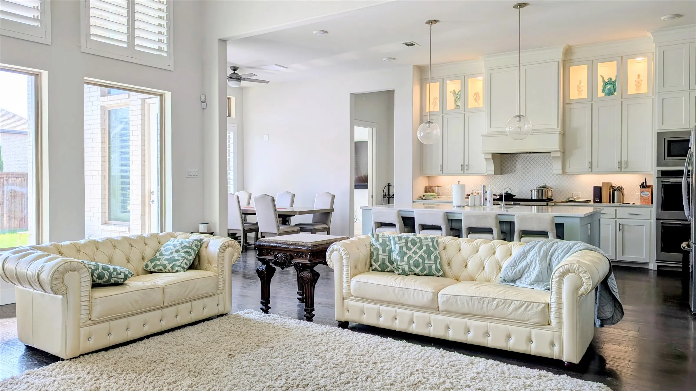 Open-concept living space featuring high ceilings, dark wood-finish flooring, and a contemporary kitchen with white cabinetry and an island with pendant lighting