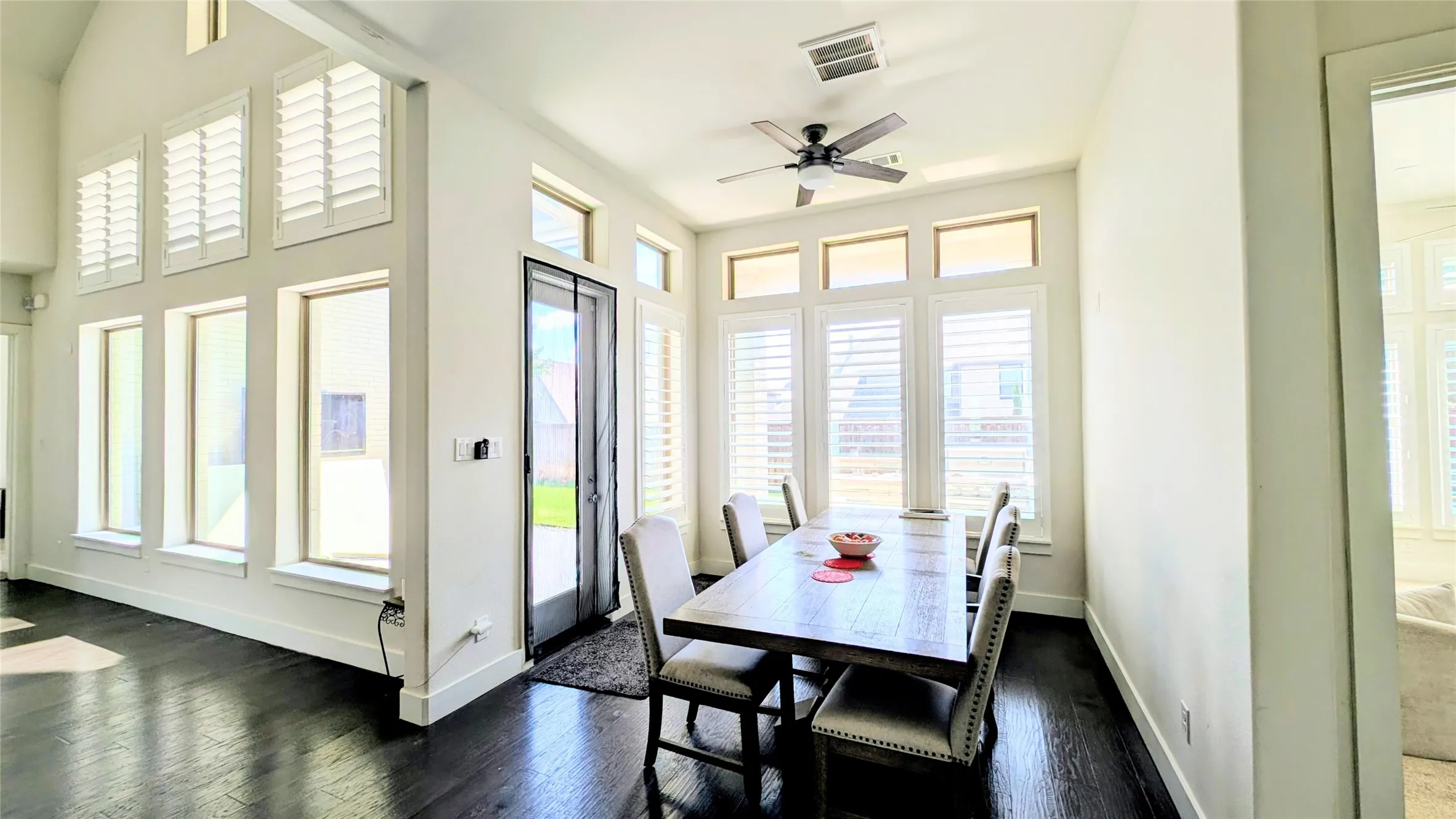 Dining area featuring dark wood-finish flooring, white plantation shutters, transom windows, and a ceiling fan with light fixture