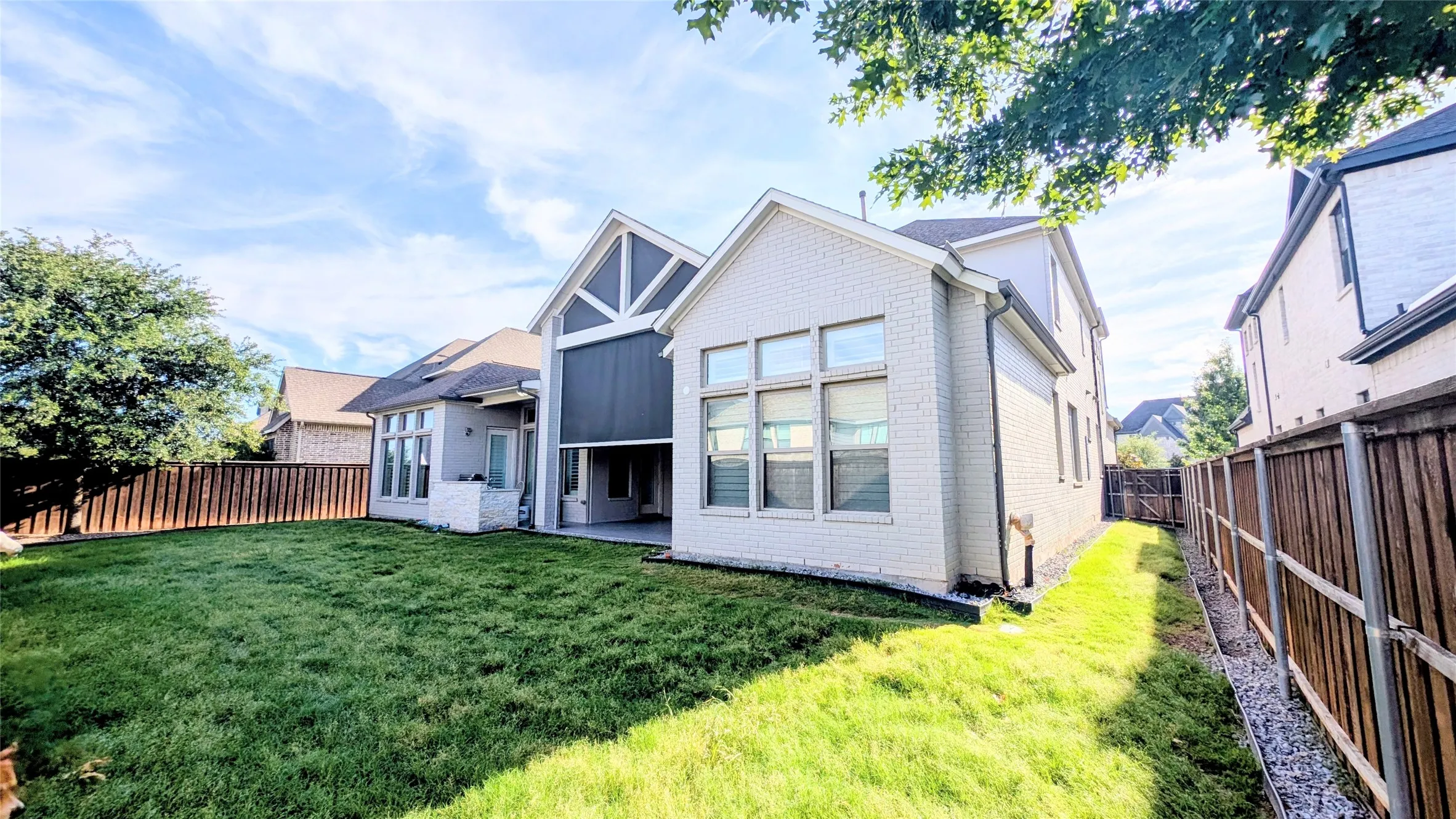 Expansive fenced backyard featuring a substantial lawn area and mature trees